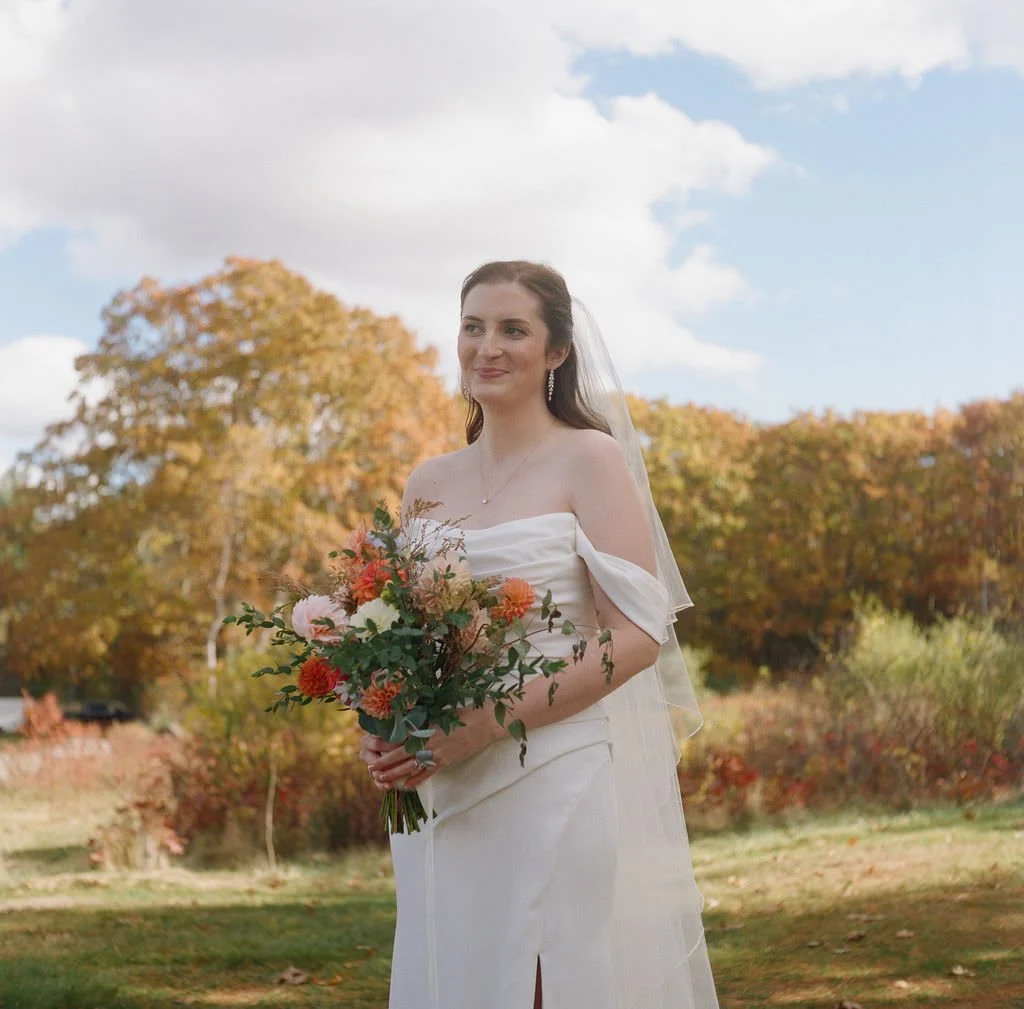Candid portrait of the bride looking off holding flowers at fall wedding outdoors in Maine