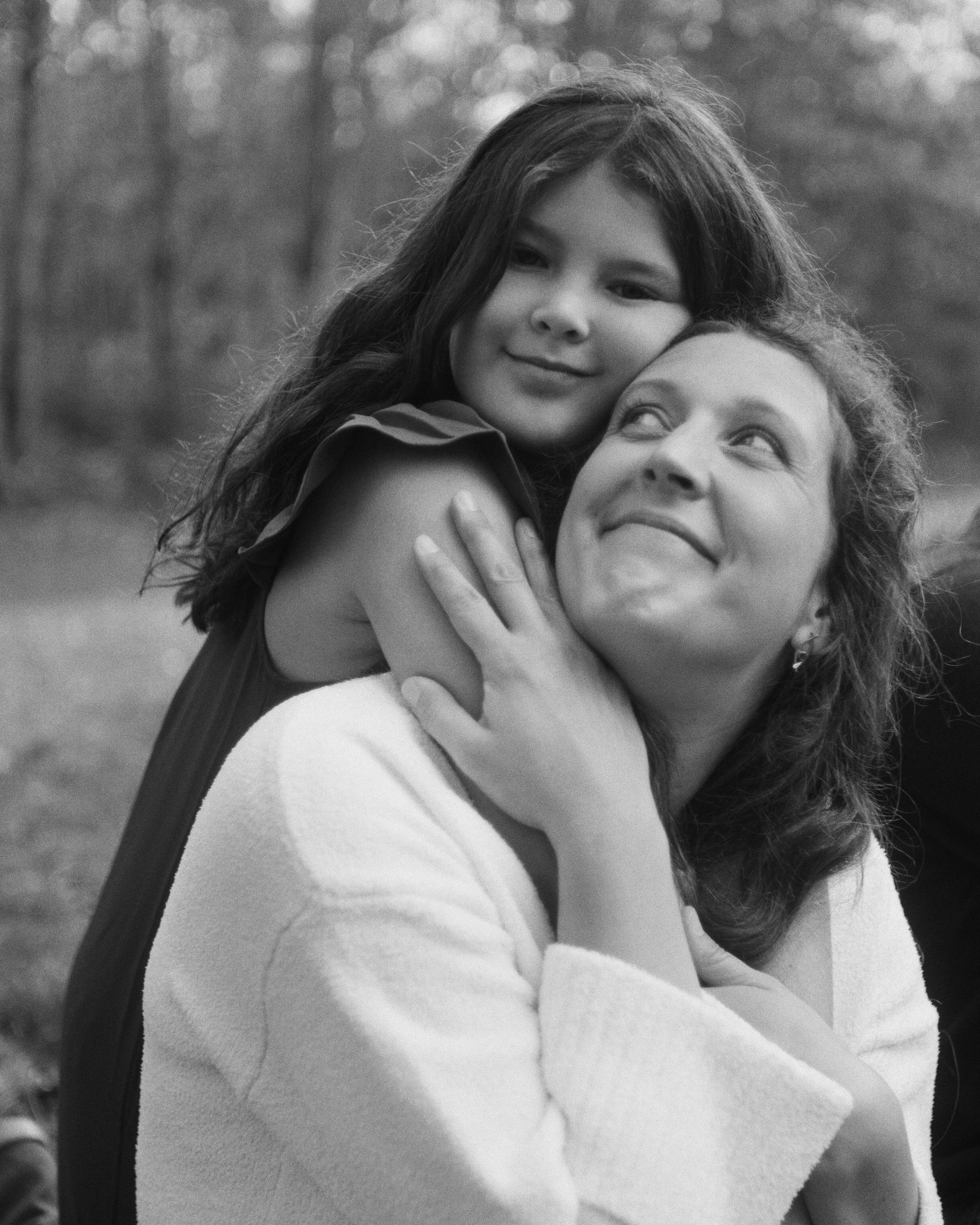 A mother looks up at her daughter snuggling with her during a backyard family photography session in Brunswick Maine
