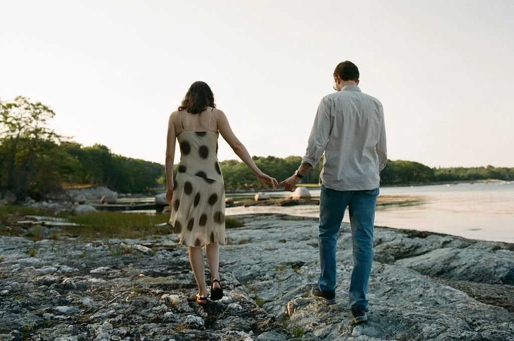 a couple walks on the rocks on a maine beach at sunset during engagement session
