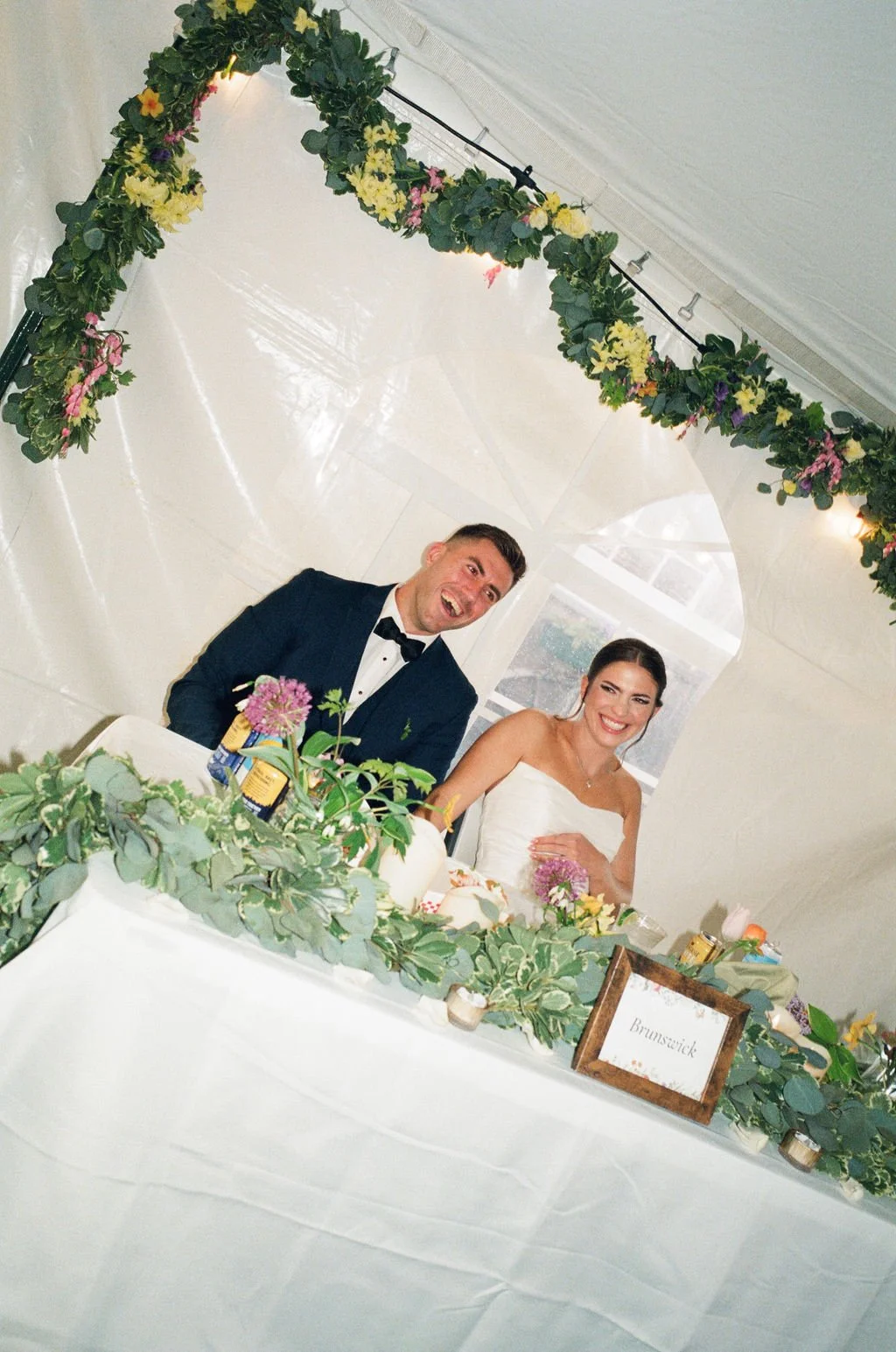 reception flash photography on film during speeches, a candid moment of the bride and groom smiling and laughing at the head table in their tent at flahertys farm in scarborough maine