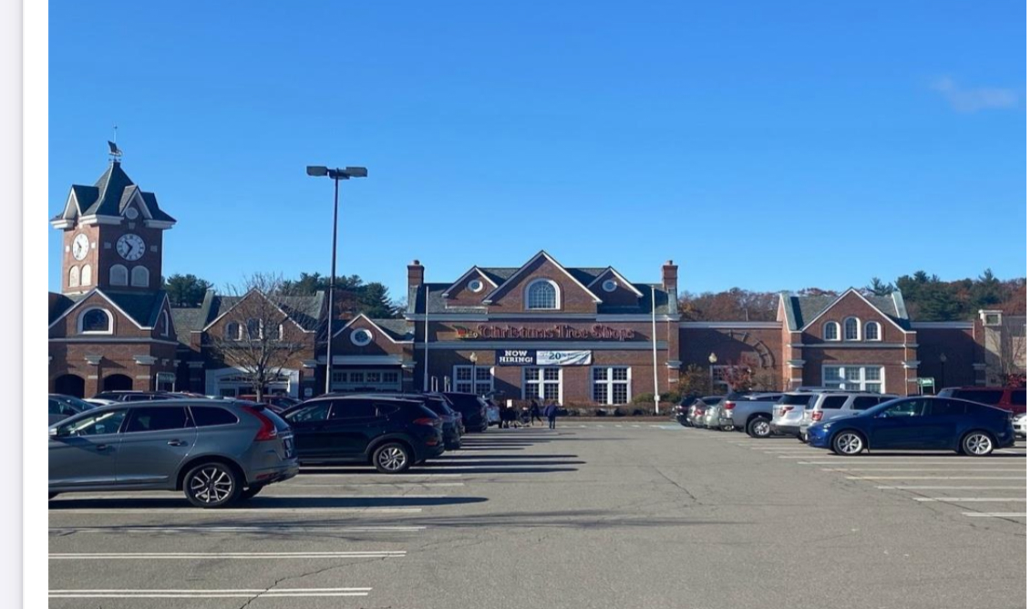 A shopping center parking lot with cars parked, a clock tower, and a building with a sign that says Christmas Tree Shop under a clear blue sky.