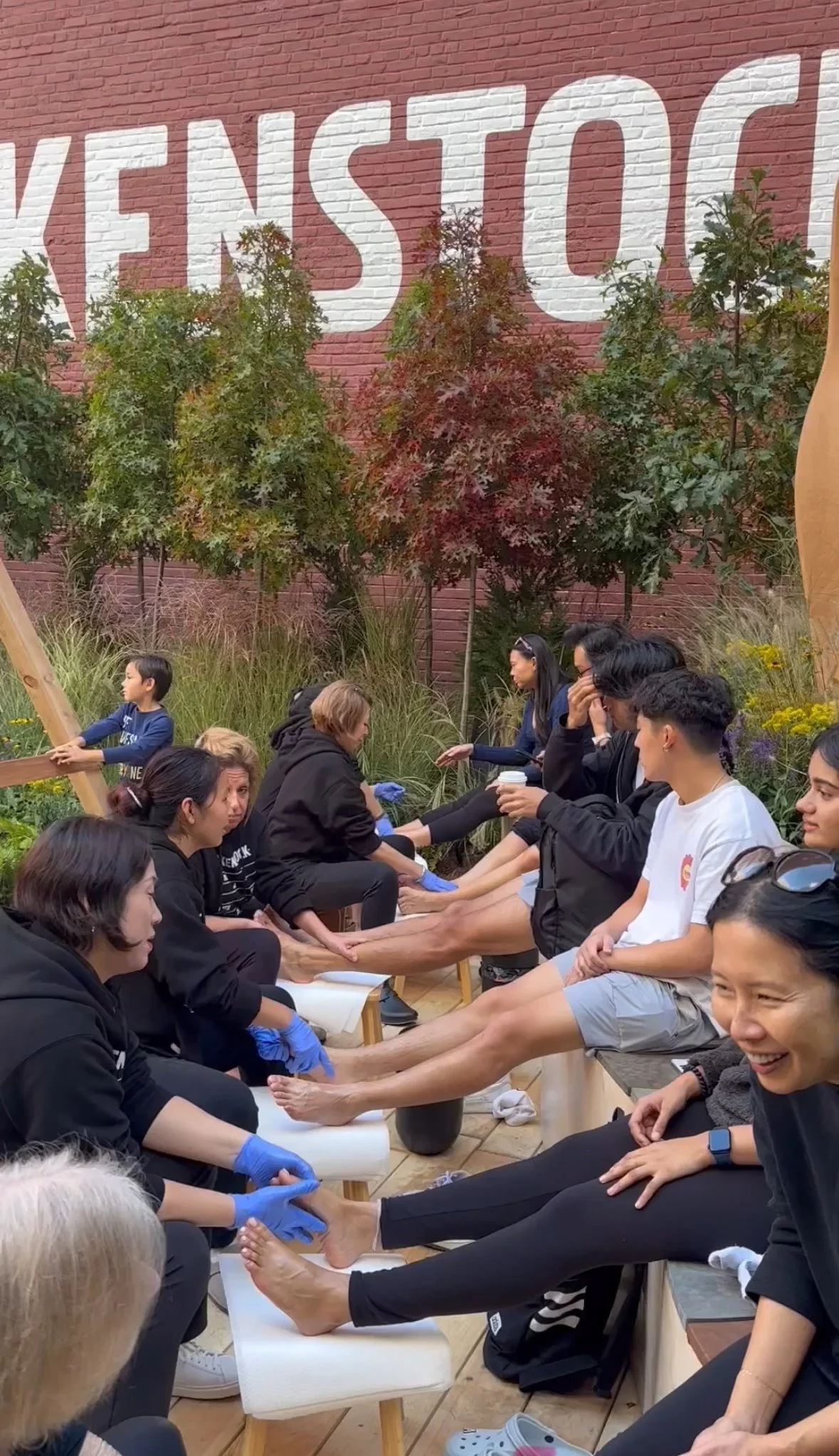 Guests enjoying relaxing foot massages outdoors at a Birkenstock event, surrounded by greenery and soft natural light on a warm day.