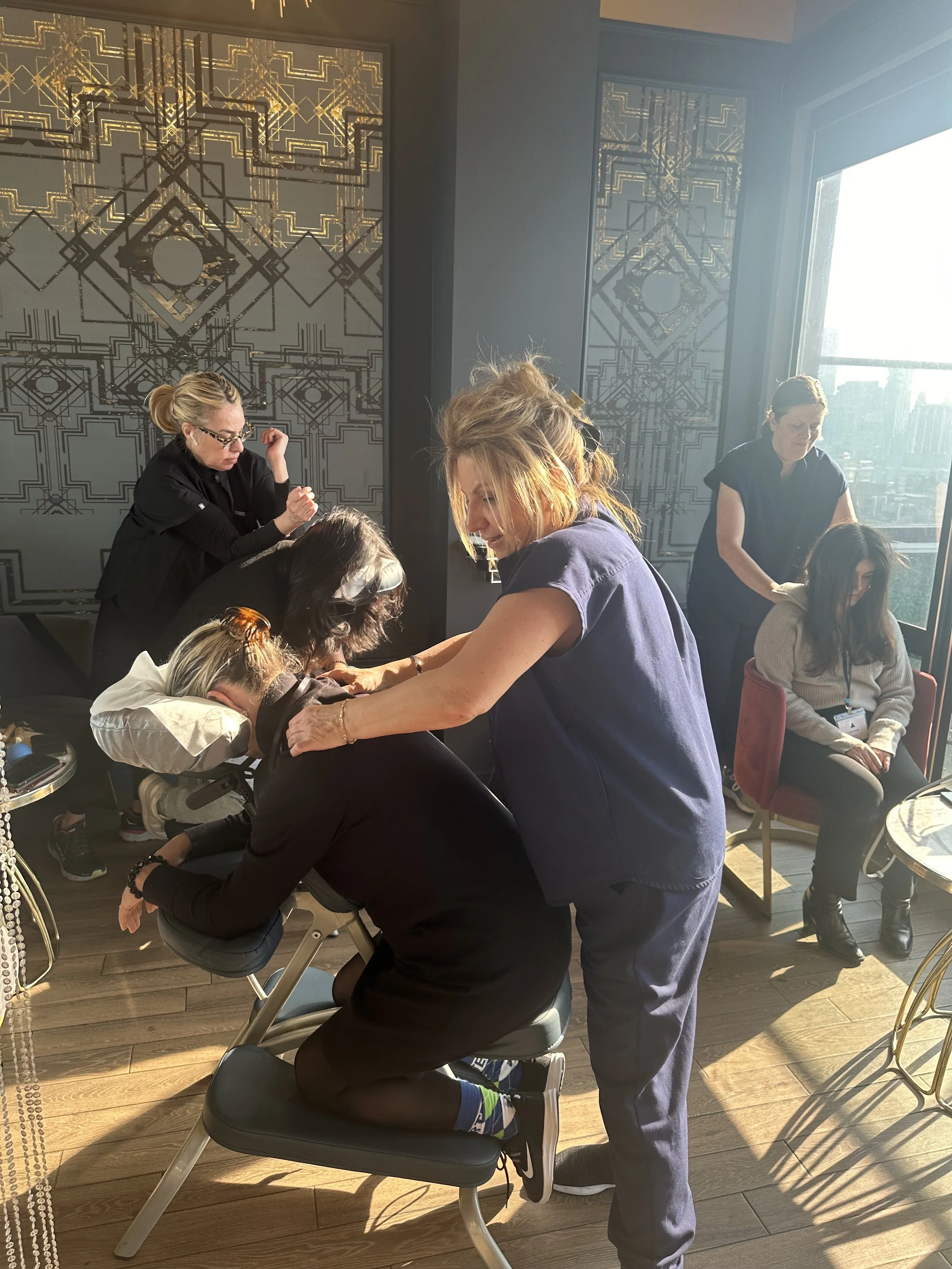 A woman receiving chiropractic or physical therapy treatment from a practitioner in a wellness or healthcare setting, with other people nearby engaged in similar activities.