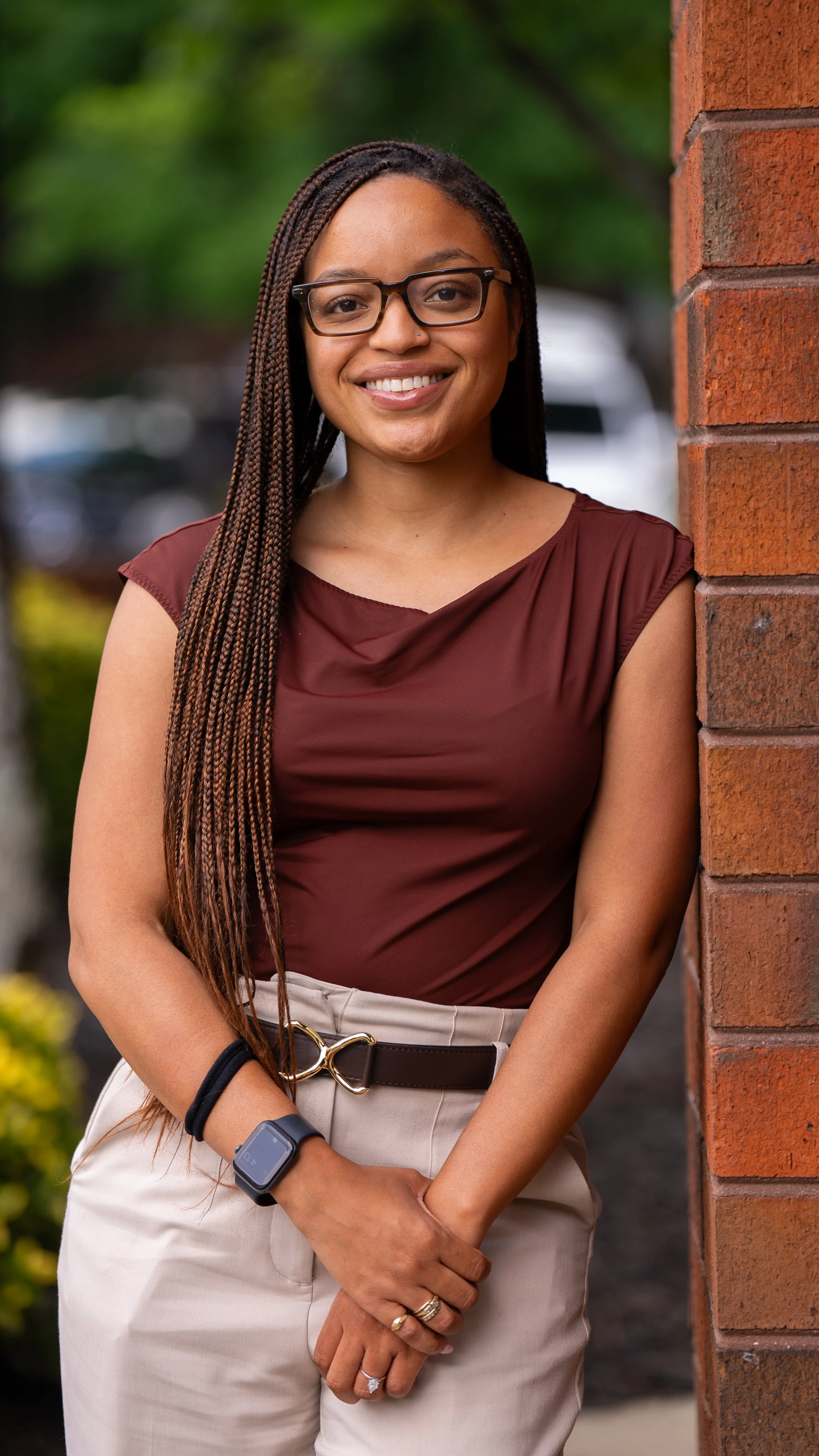 Headshot of LaShonda Procter, Clinical Advocate at PAD. LaShonda has long braids, glasses, and a maroon top and is standing outdoors, next to a brick wall, smiling.