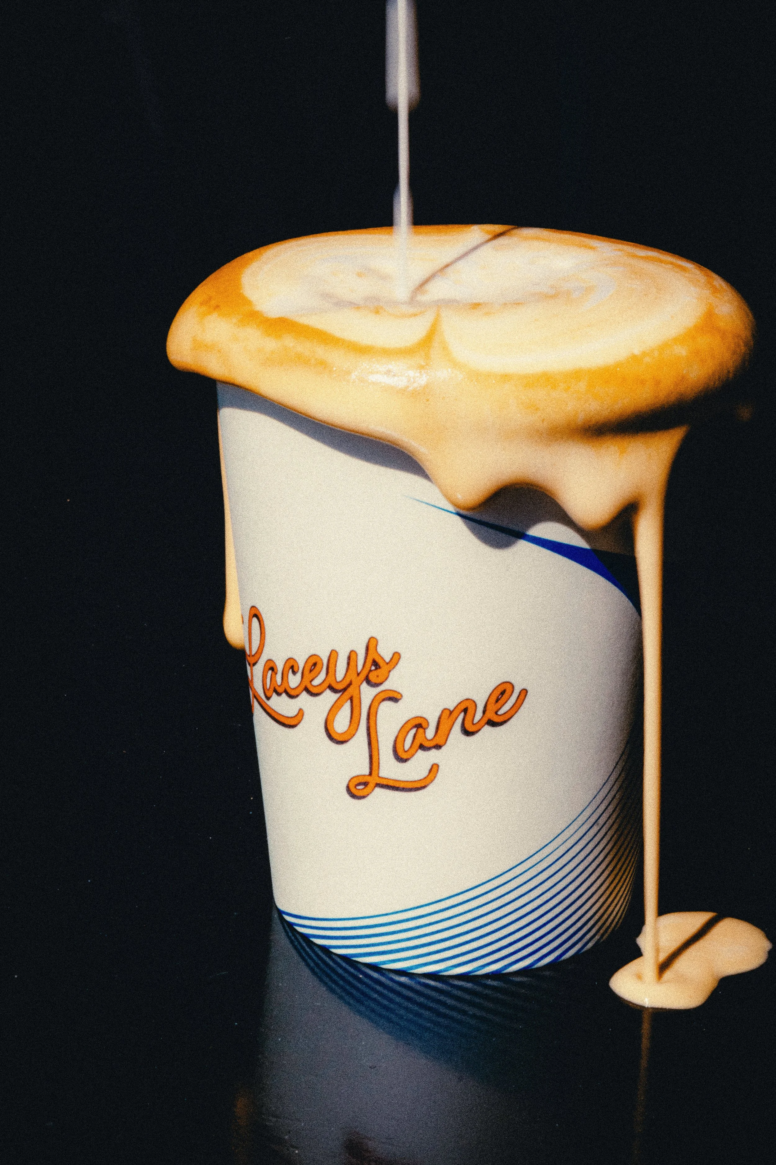 Close-up of a creamy latte being poured into a white cup labeled “Laceys Lane".