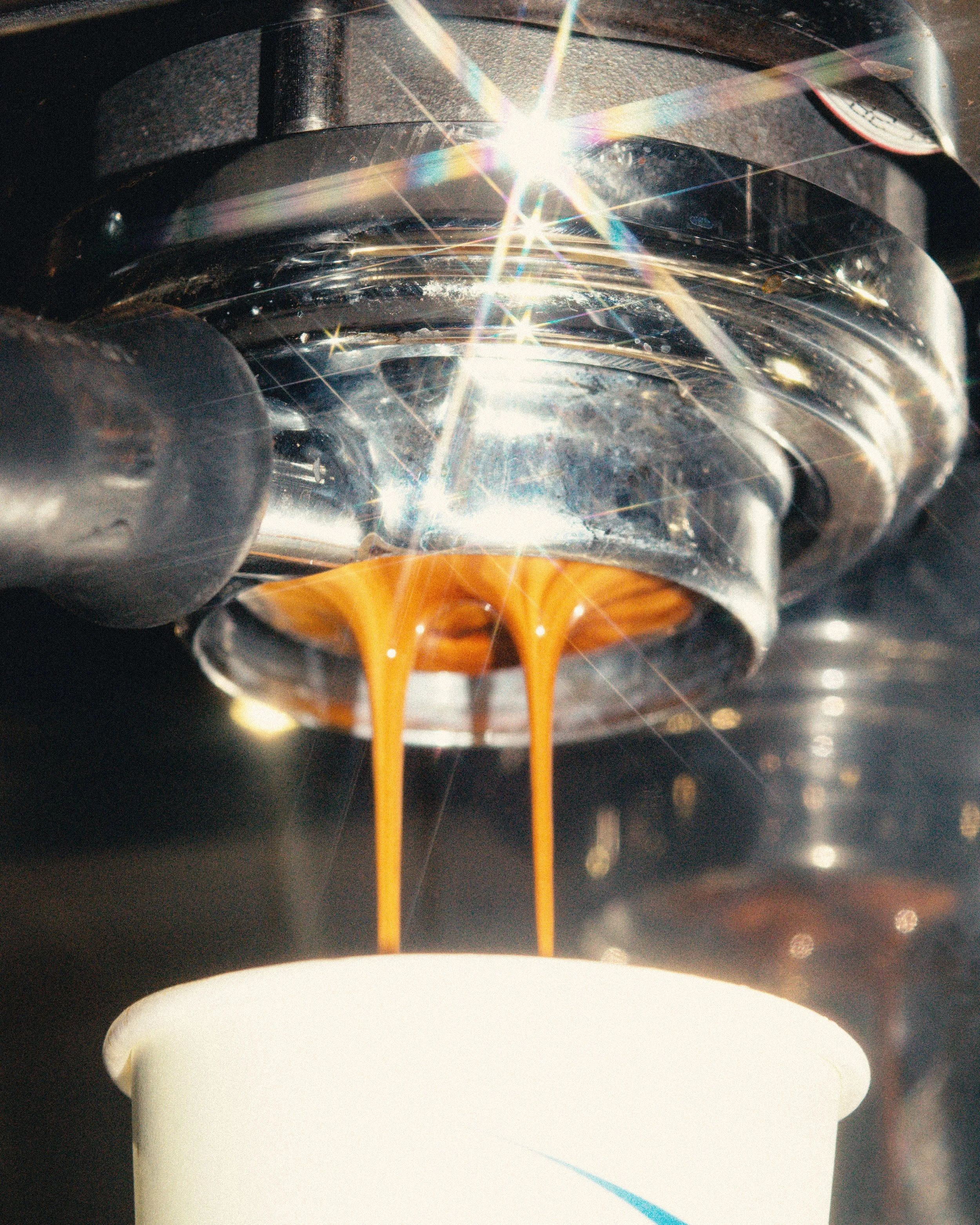 Close-up of a espresso extracting into a paper takeaway cup with dramatic light flares.
