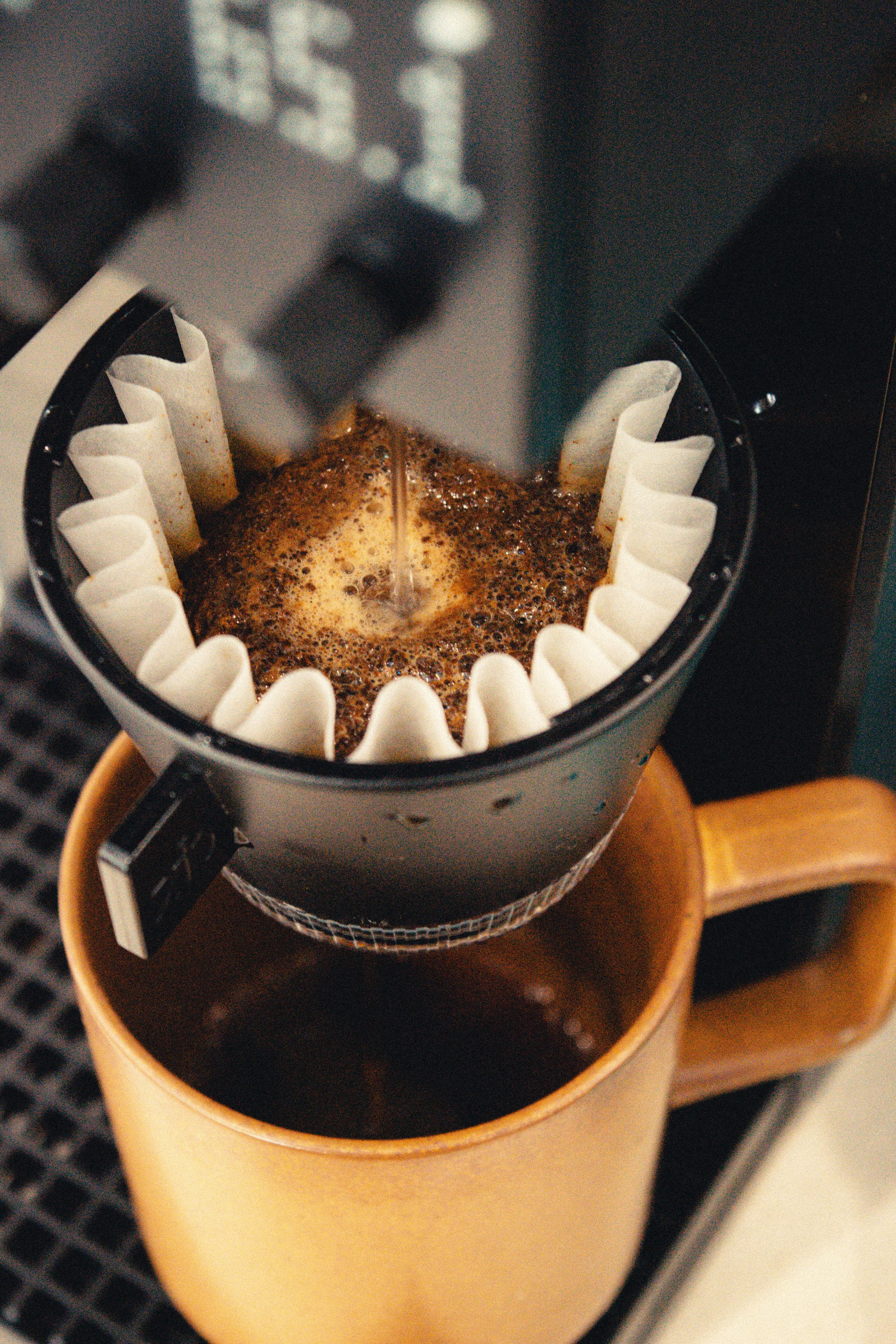 Close-up of a coffee dripper brewing filter coffee into a cup, surrounded by white paper filter folds.