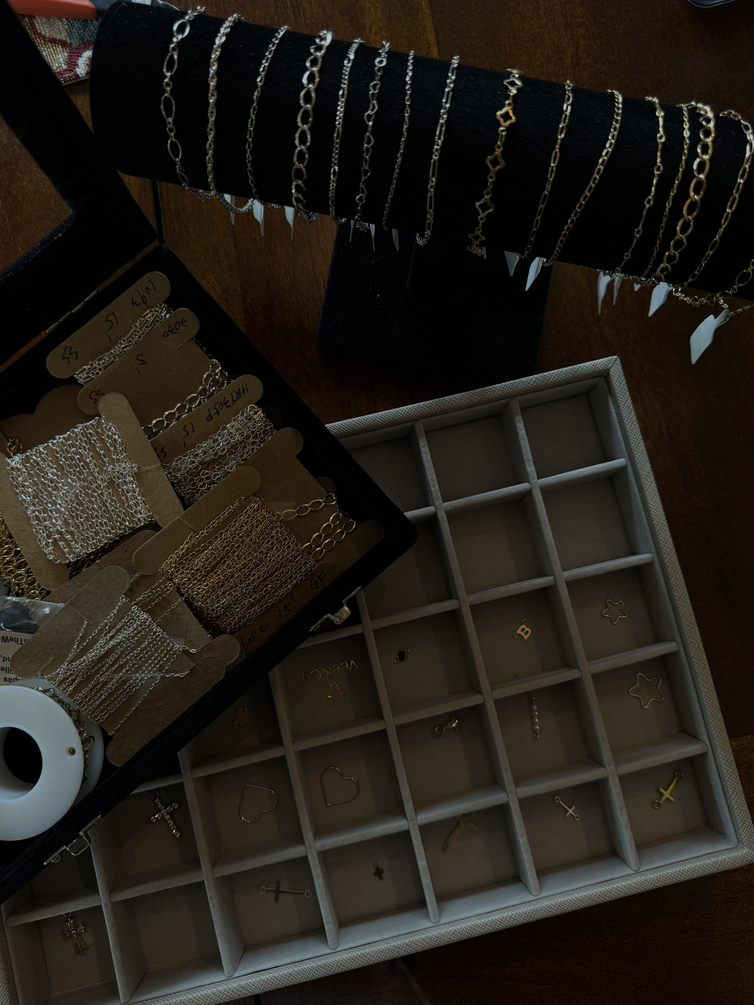 Jewelry display with various bracelets hanging on a black stand, open jewelry box with compartments containing small jewelry items, and a collection of hoop and chain earrings on cardboard cards.