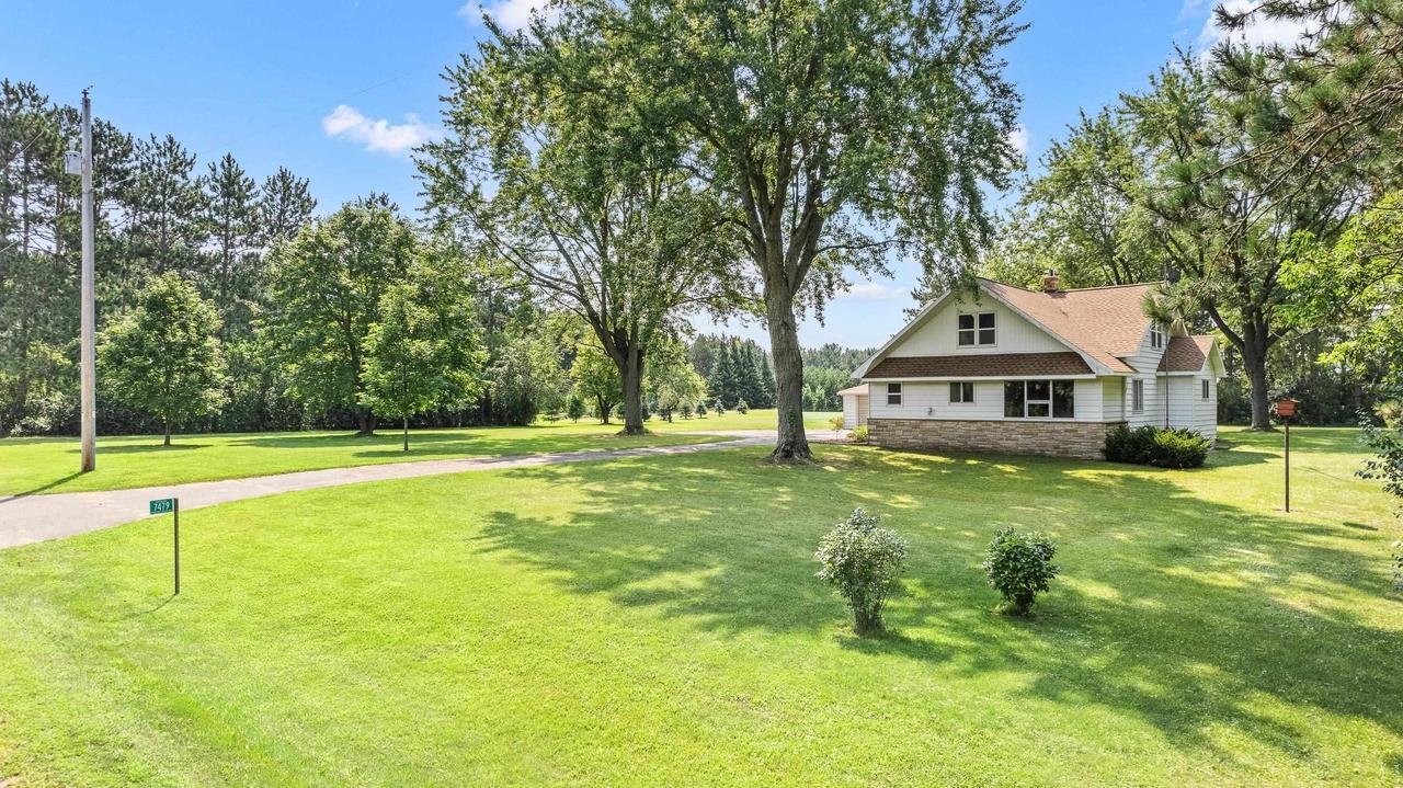 House with large lawn, surrounded by trees and clear blue sky.