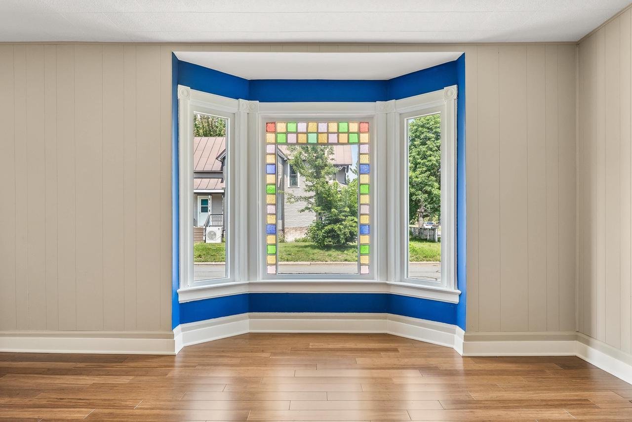 Bay window with colorful stained glass, beige walls, blue trim, and wooden floor.