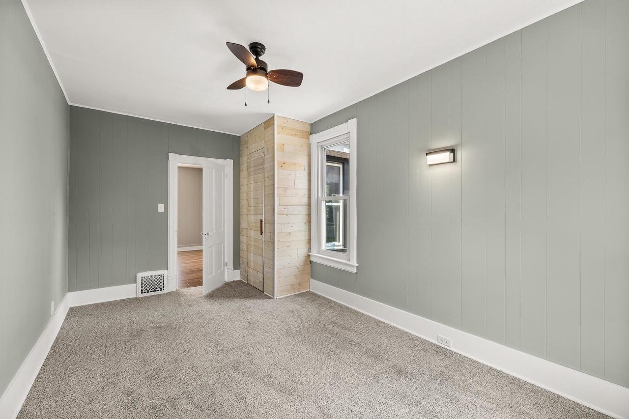 Empty room with gray walls, beige carpet, white trim, wooden closet, ceiling fan, and window.