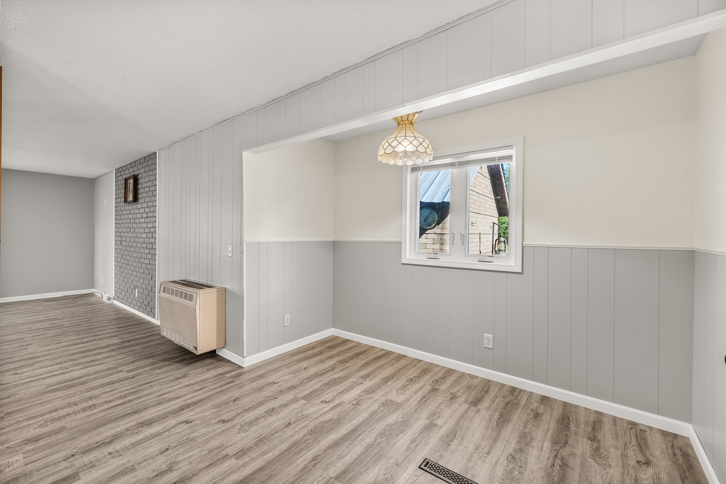 Empty room with gray walls, wood flooring, a window, and a wall heater.