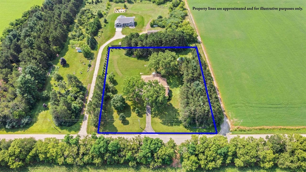Aerial view of a rural property with trees and grass, outlined in blue, displaying a driveway leading to a house. Surrounding areas feature additional greenery and a road.