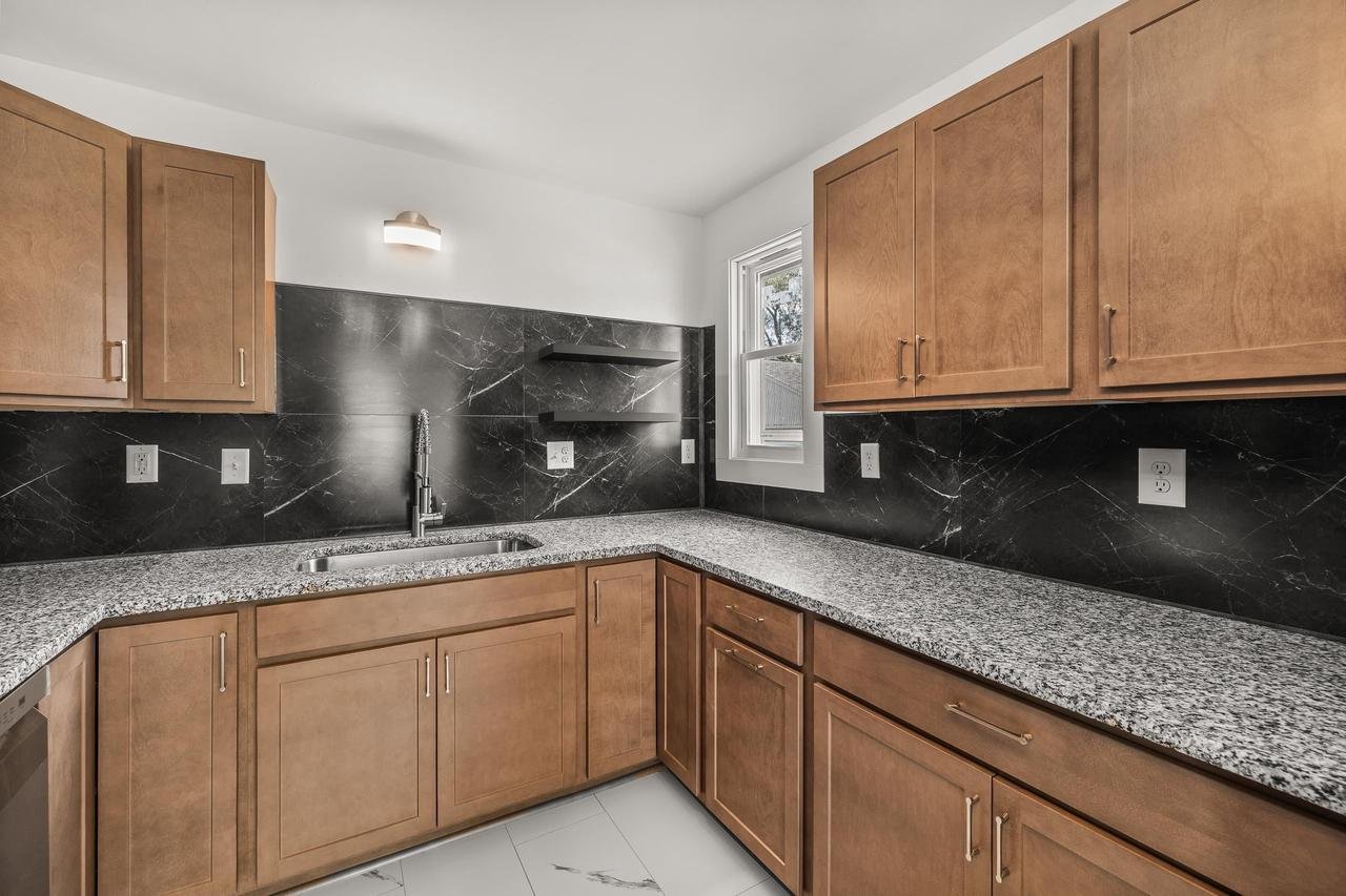 Modern kitchen with wooden cabinets, granite countertops, and black marble backsplash.