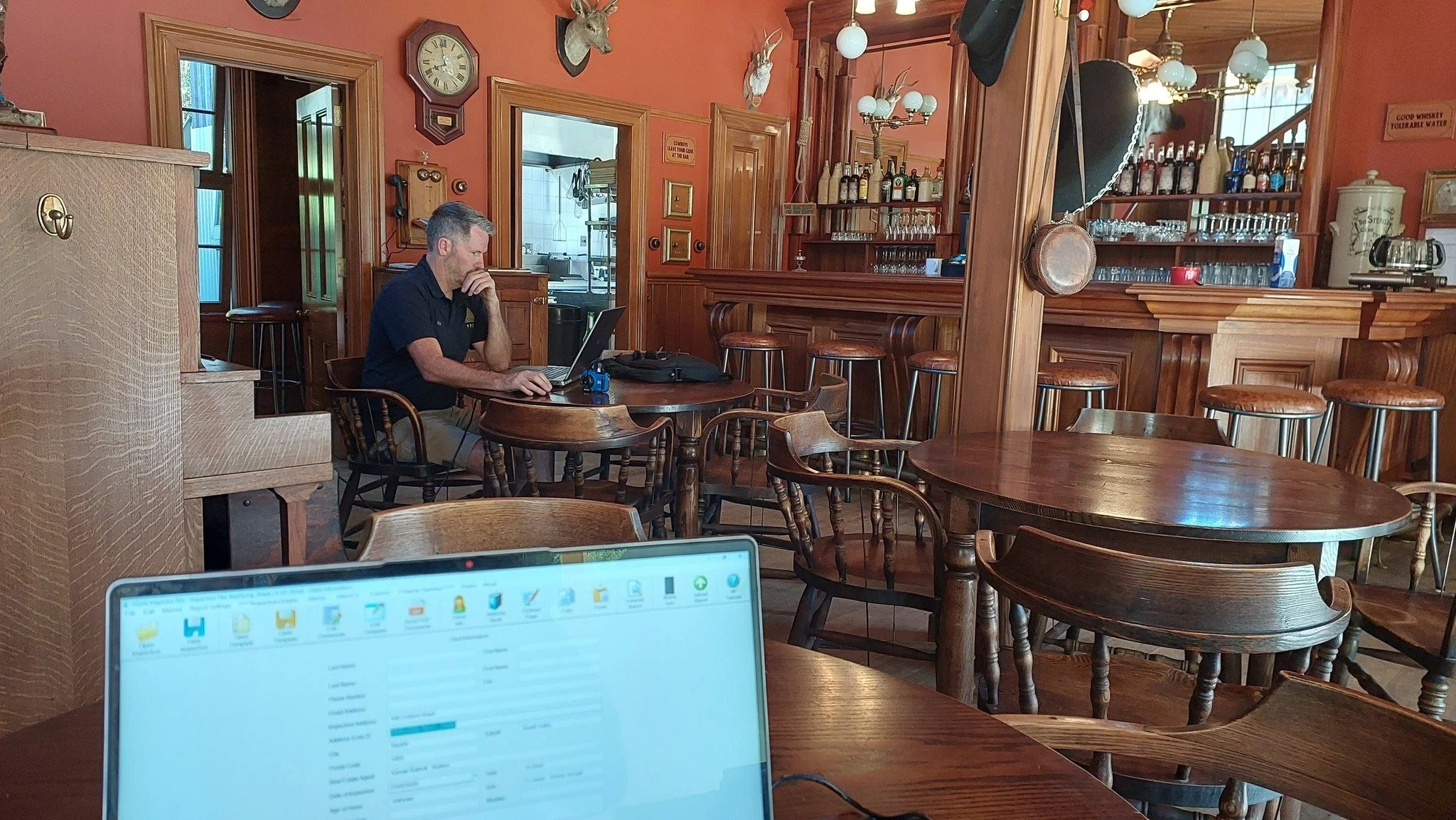Hayden Nottingham working on a property inspection at a property that is for sale. The property includes a bar has wooden paneling, barstools, and decorative mounted animal heads on the wall.