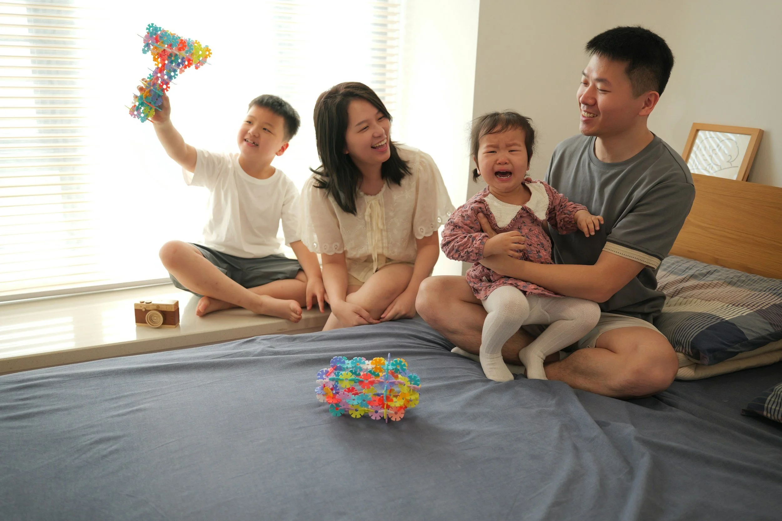 Two parents and two young children sitting together on a bed playing, representing early family environments explored in childhood trauma therapy in Virginia