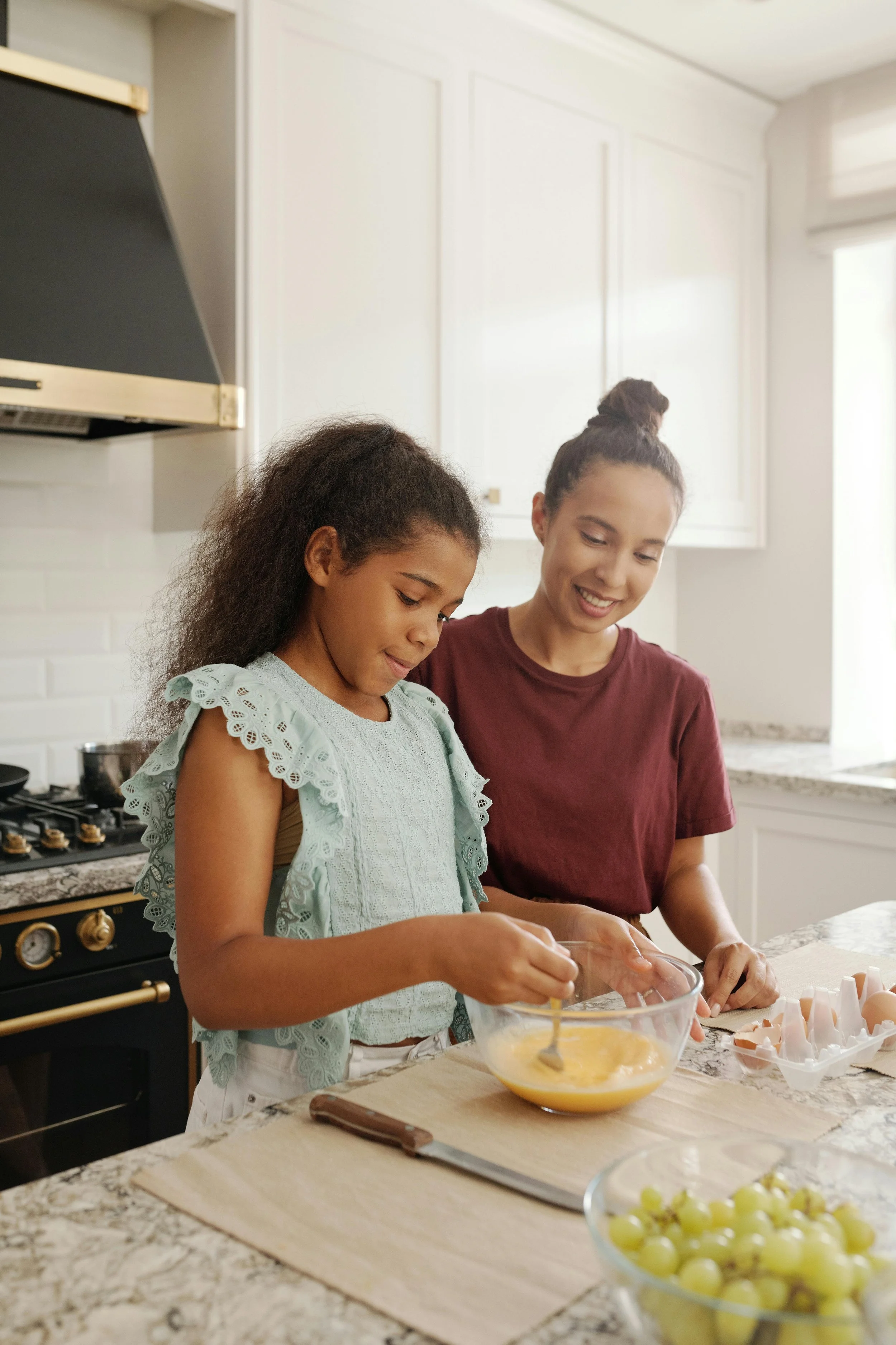 Mother and young daughter cooking together in the kitchen, representing family dynamics explored in childhood trauma therapy in Northern Virginia