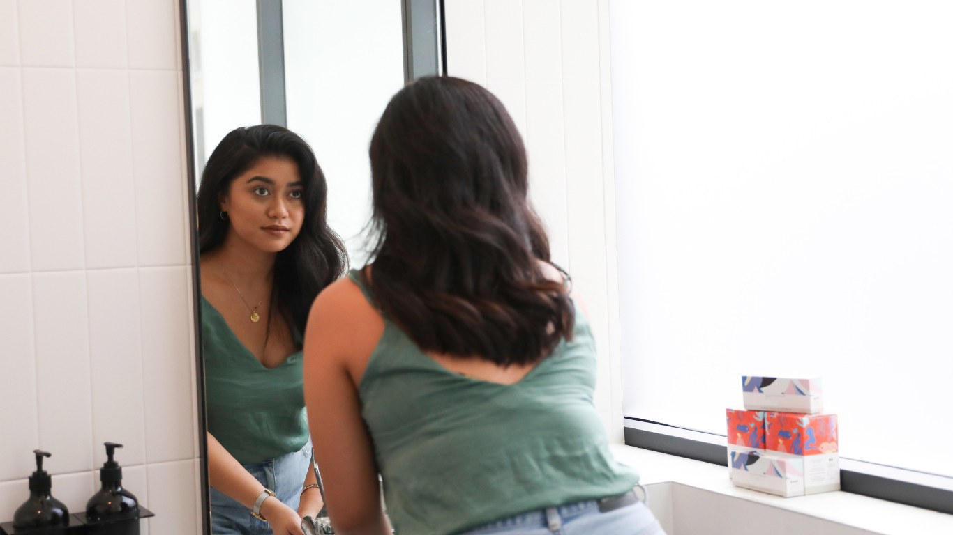 Woman standing at a mirror washing her hands, representing the self-awareness and reflection explored in trauma therapy in Northern Virginia