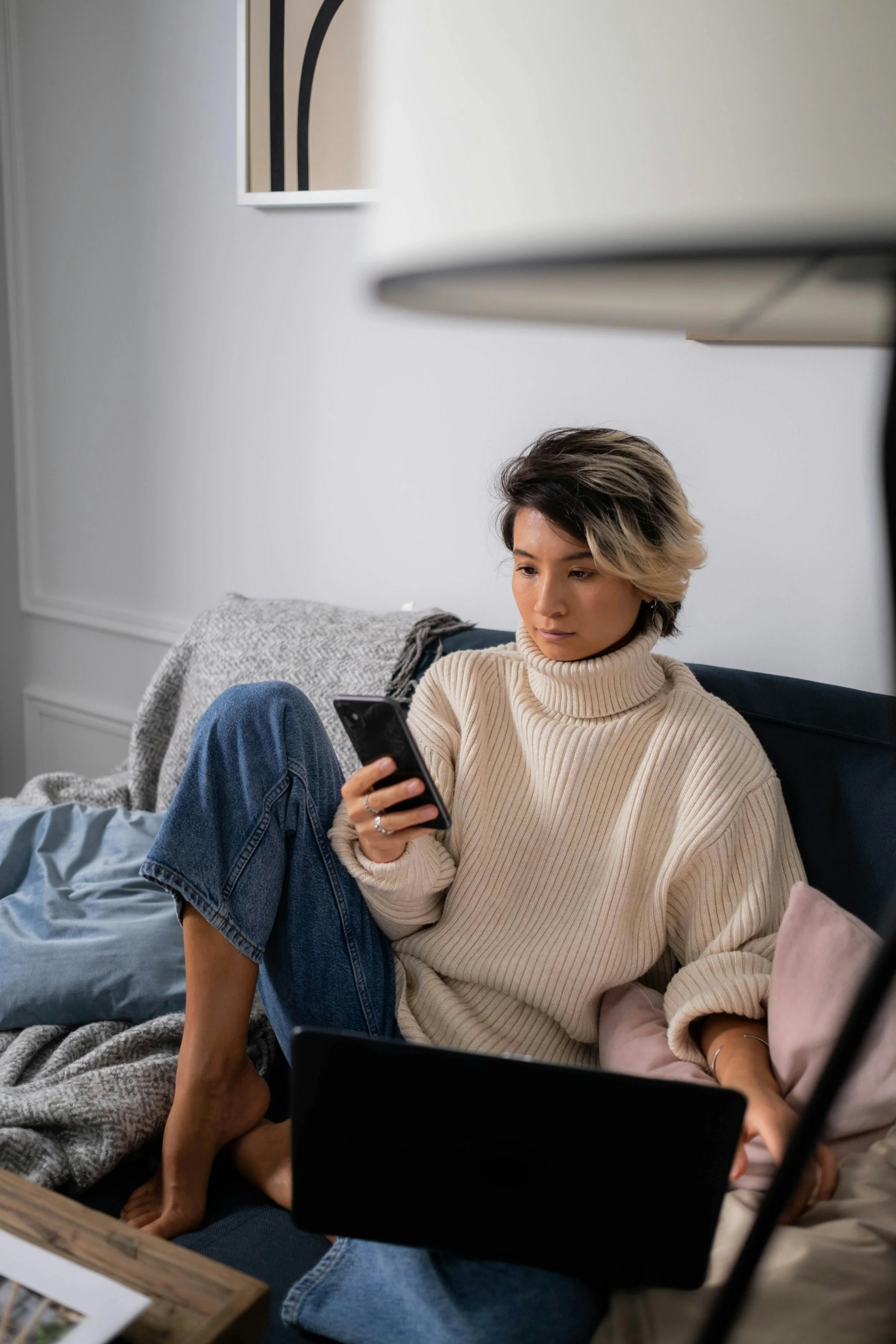 Woman sitting on a couch with a laptop and phone, representing telehealth EMDR therapy available to clients in Virginia and Maryland
