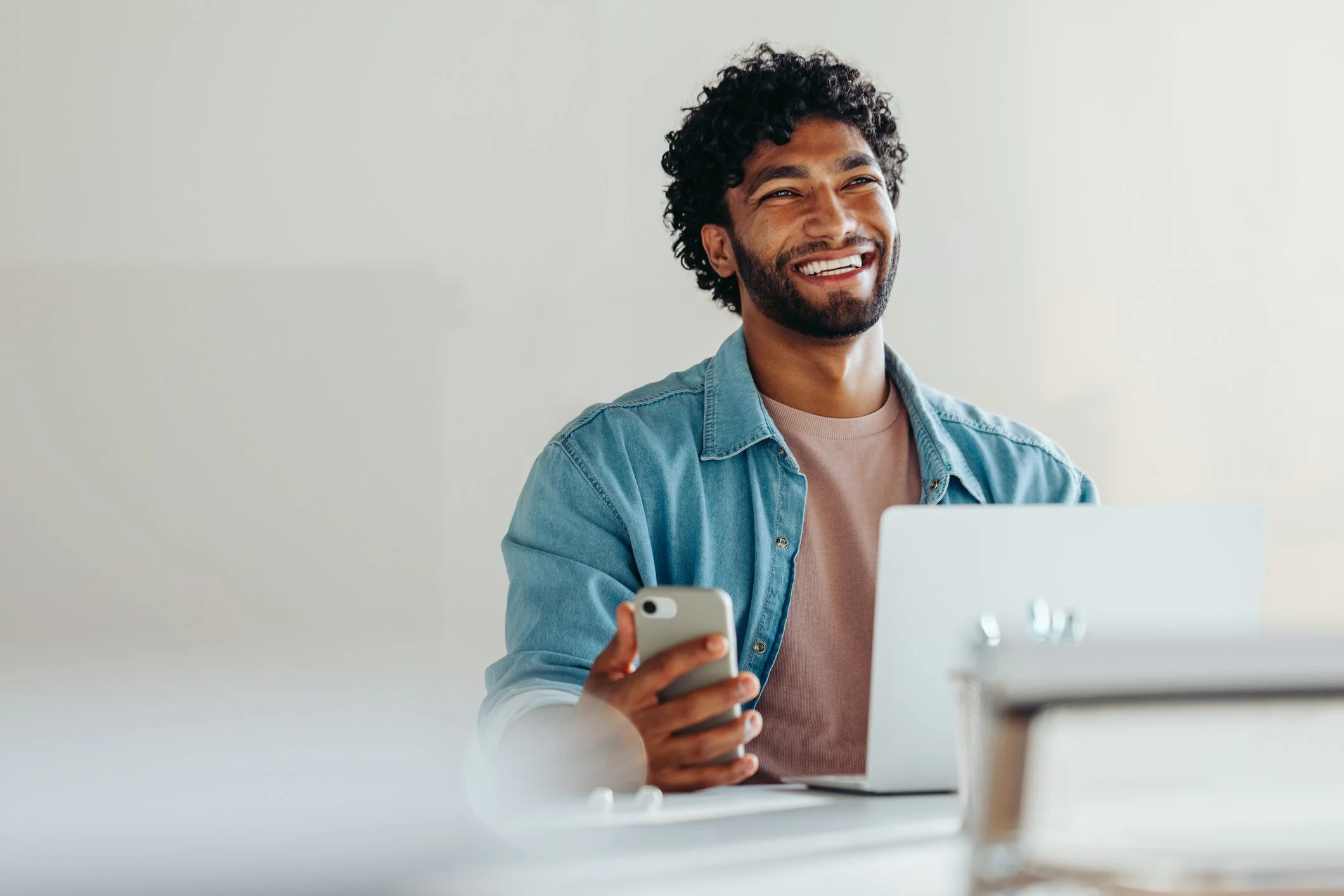 Man sitting at a desk smiling with his phone in hand and a laptop open, representing progress and confidence through anxiety therapy for high-achieving adults in Virginia