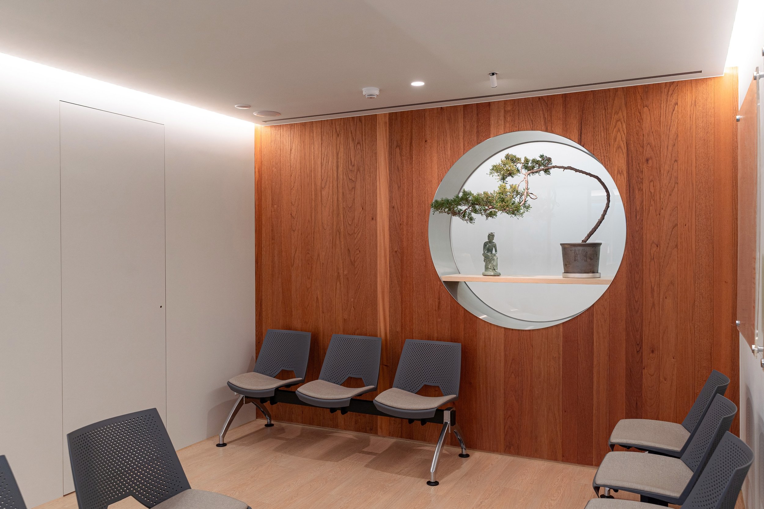 診所候診區設有灰色座椅與木質牆面，圓形壁龕中展示盆栽與裝飾雕像，營造安靜放鬆的等候空間。