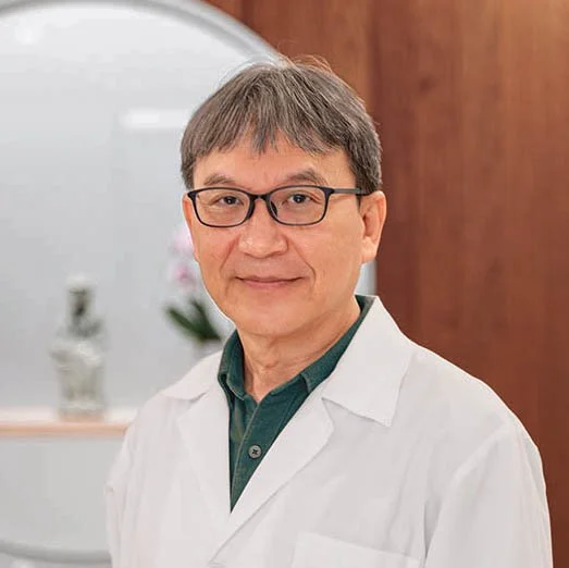 中醫師於診所內的專業肖像照，身穿白袍，呈現親切可信賴的醫療形象。