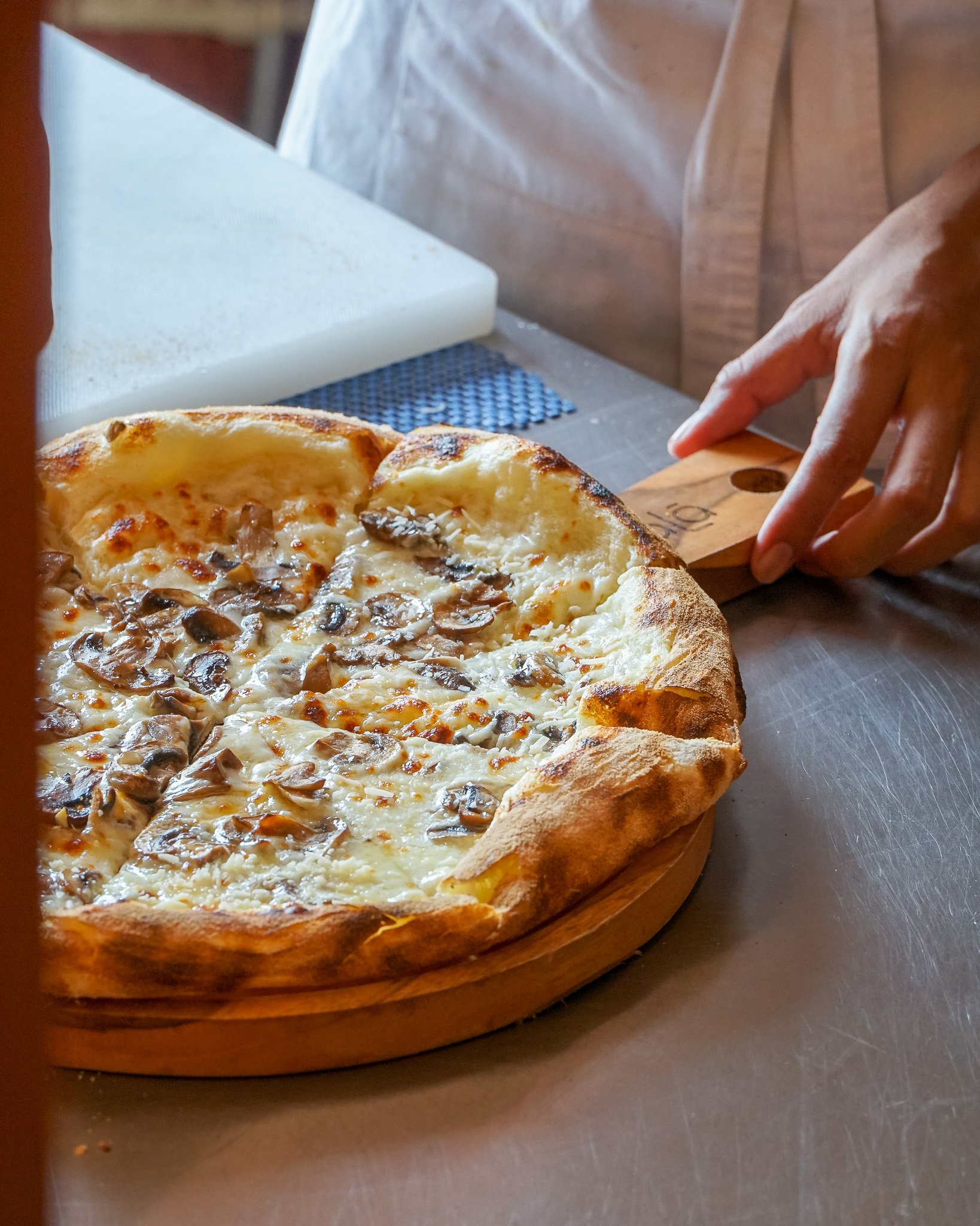 A freshly baked pizza with mushrooms on a wooden pizza board.