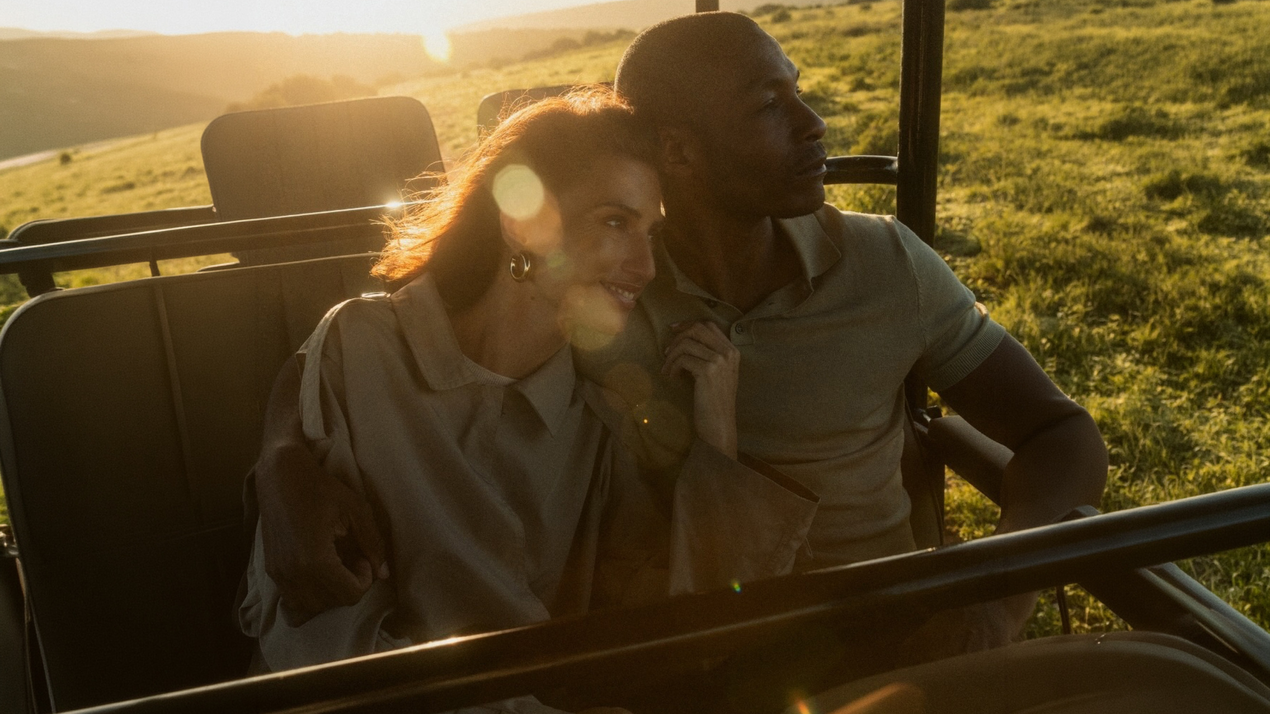 A man and a woman sitting together in a golf cart during sunset in a grassy field, smiling and enjoying each other's company.