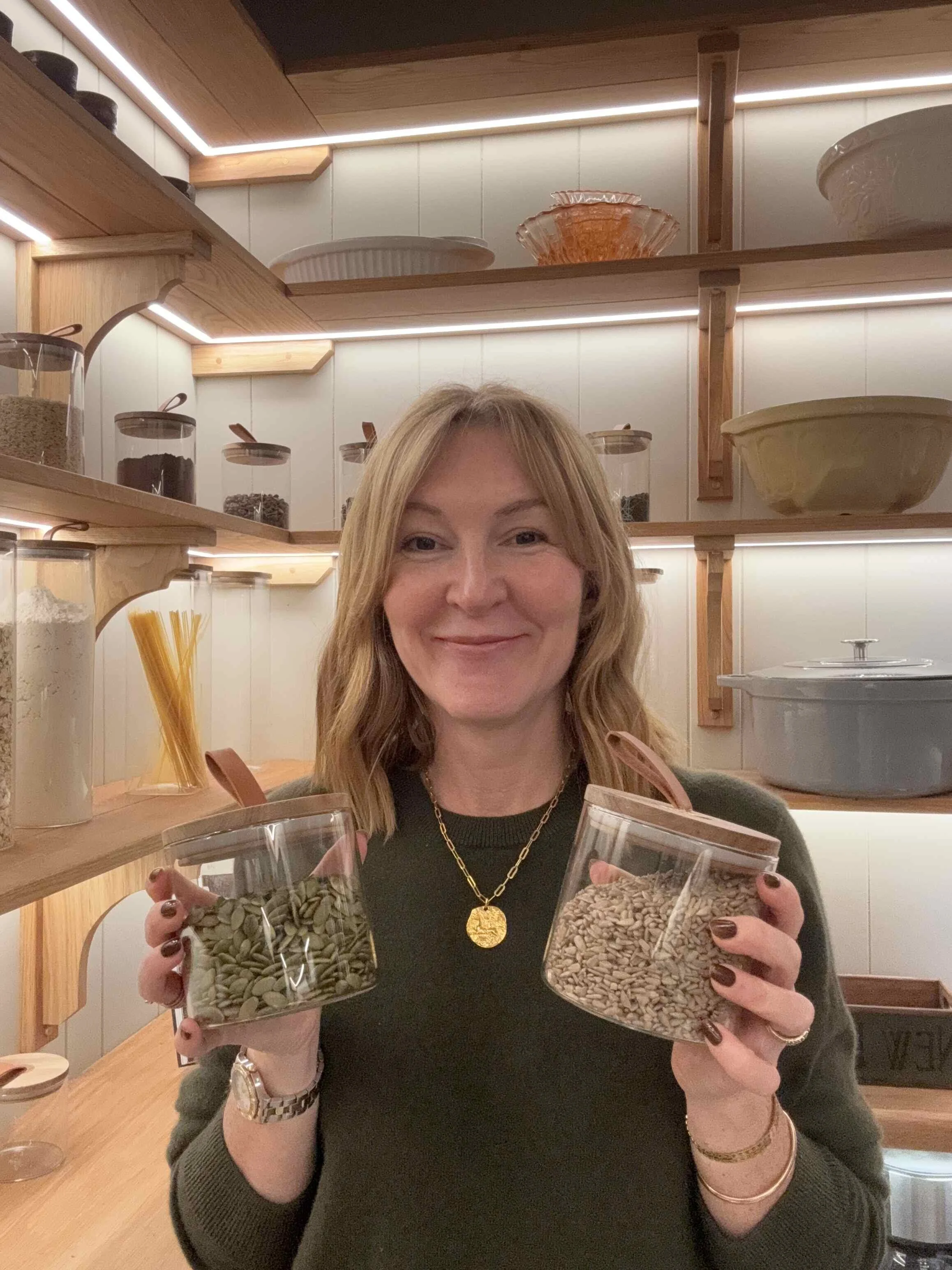 Lindsey Whitaker holding containers of seeds in a warm, organized kitchen, reflecting her hands-on, nourishing approach to midlife wellness workshops and retreats.