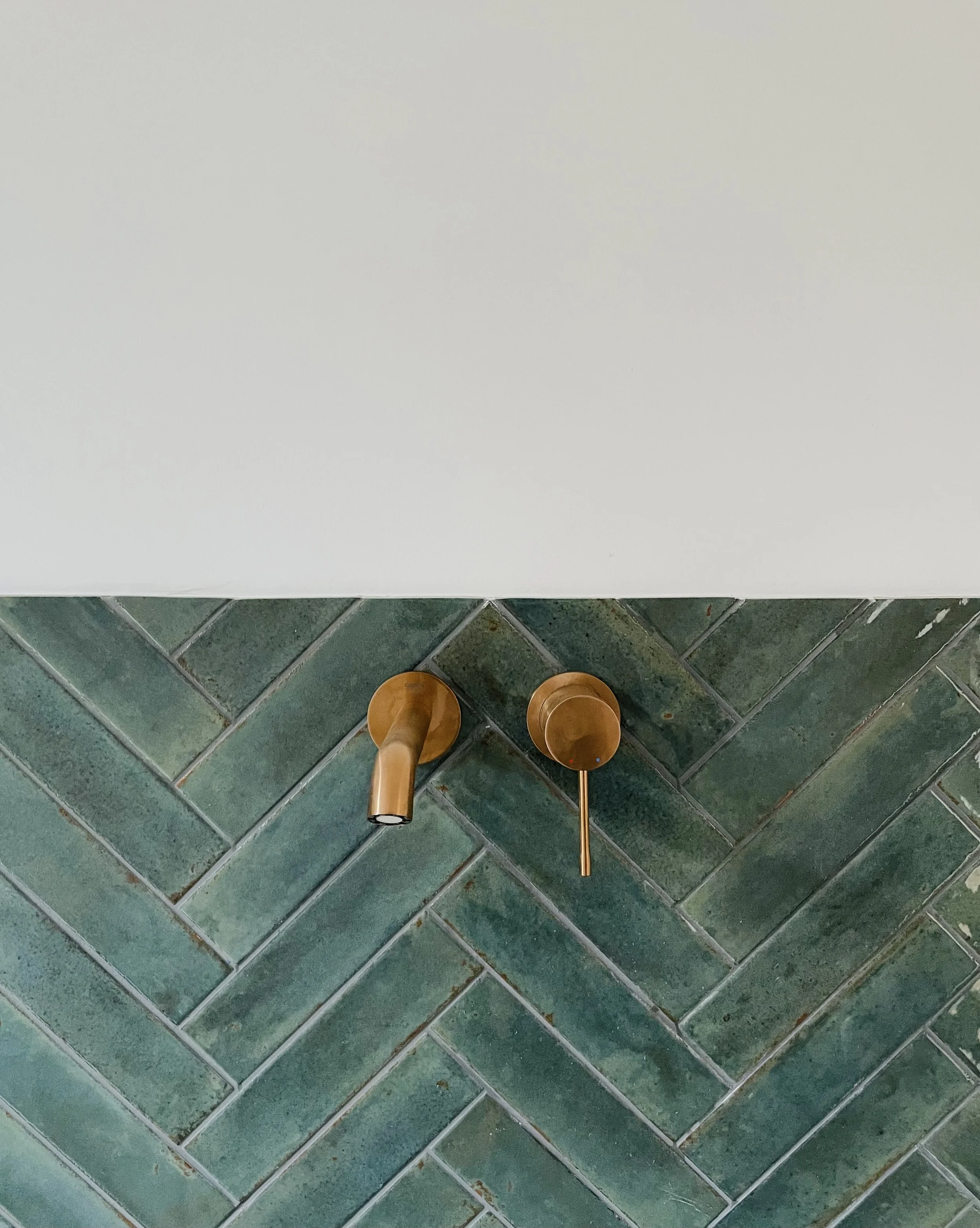 Braune Wasserhähne an einer grünlich glasierten Fliesensäule in einem Badezimmer.