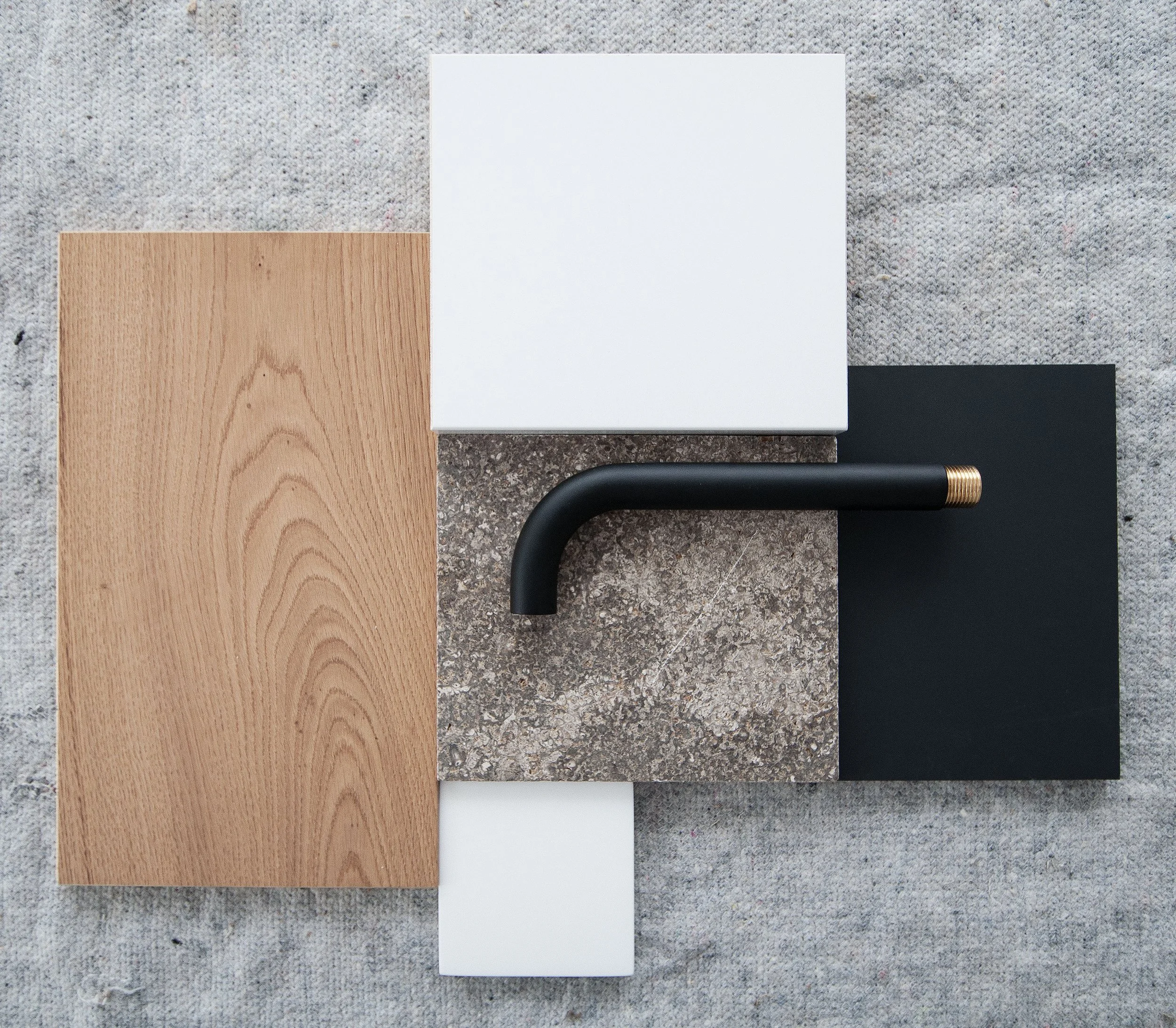 Verschiedene Materialproben und ein schwarzer Wasserhahn liegen auf einem grauen Stoff Untergrund.