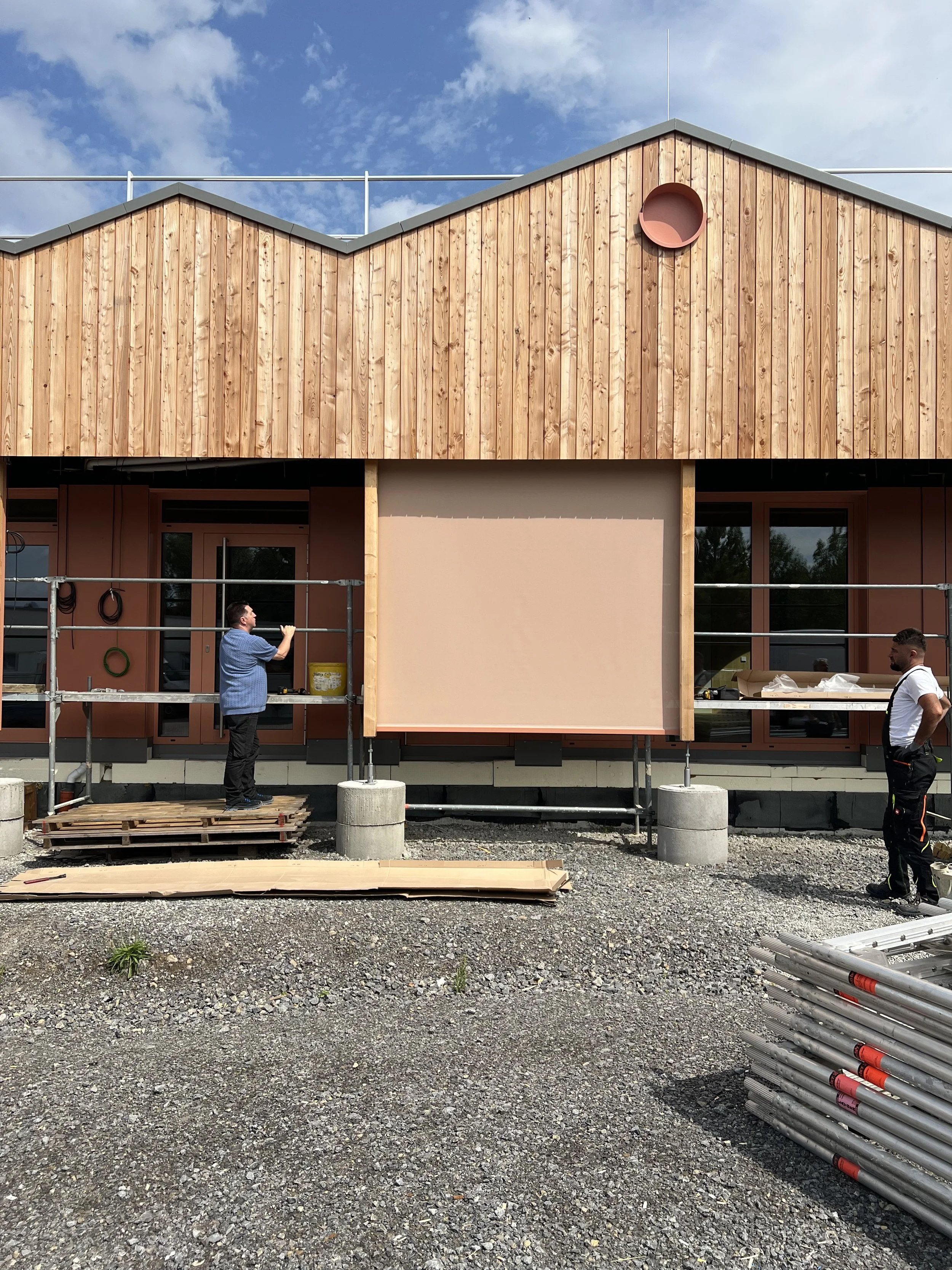 Ein im Bau befindliches Gebäude mit Holzfassade und zwei Arbeitern, die bei der Konstruktion während des Tages arbeiten.