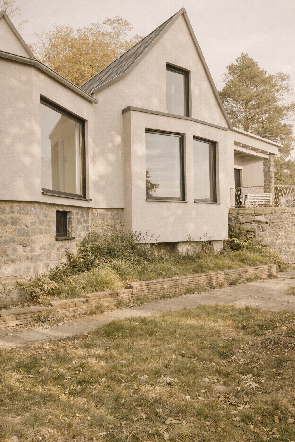 Ein modernes Haus mit großen Fenstern, einer Steinmauer am Sockel und einem kleinen Garten vor dem Haus.