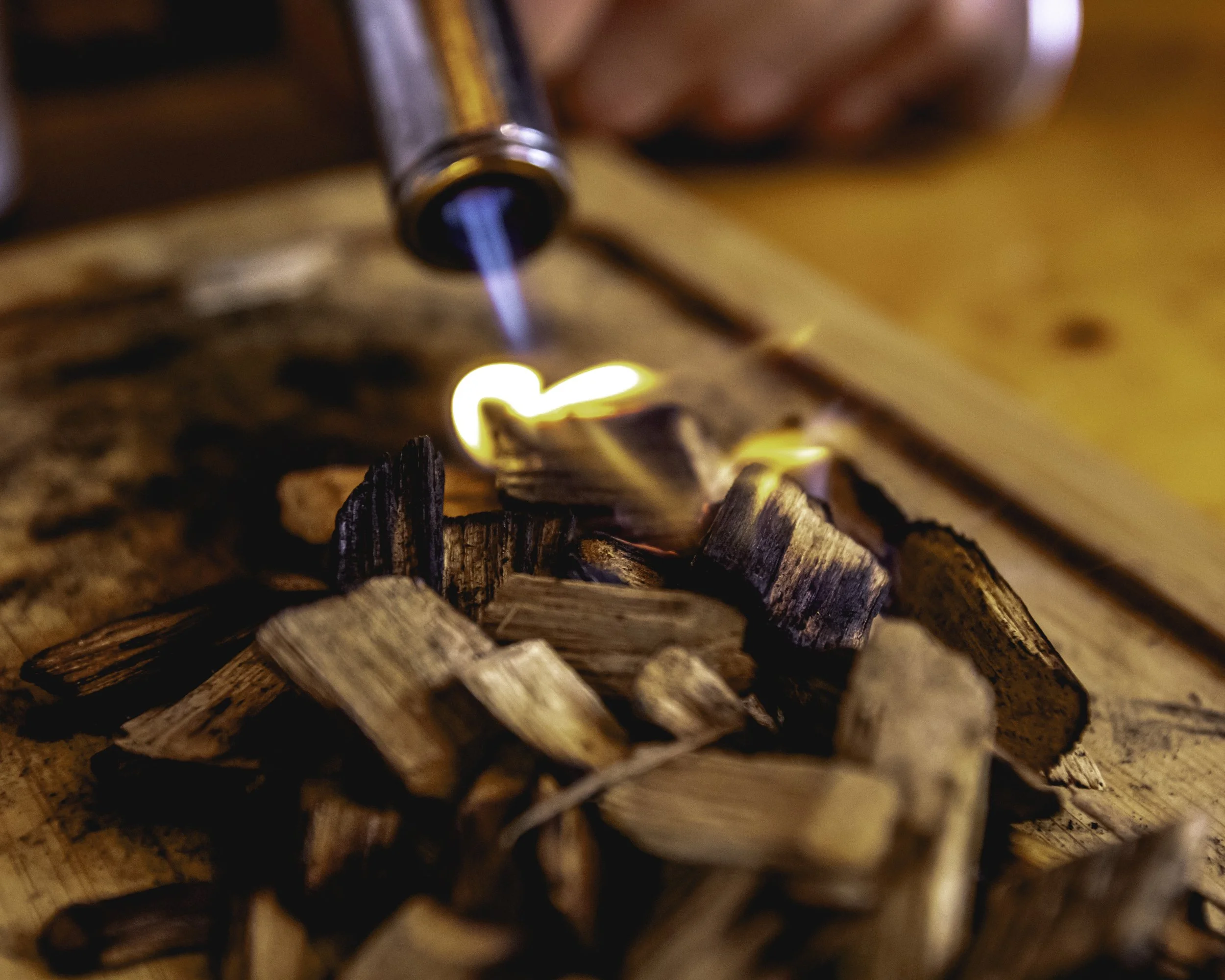 Close-up of wooden firewood pieces on a fire pit with a lighter igniting flames.