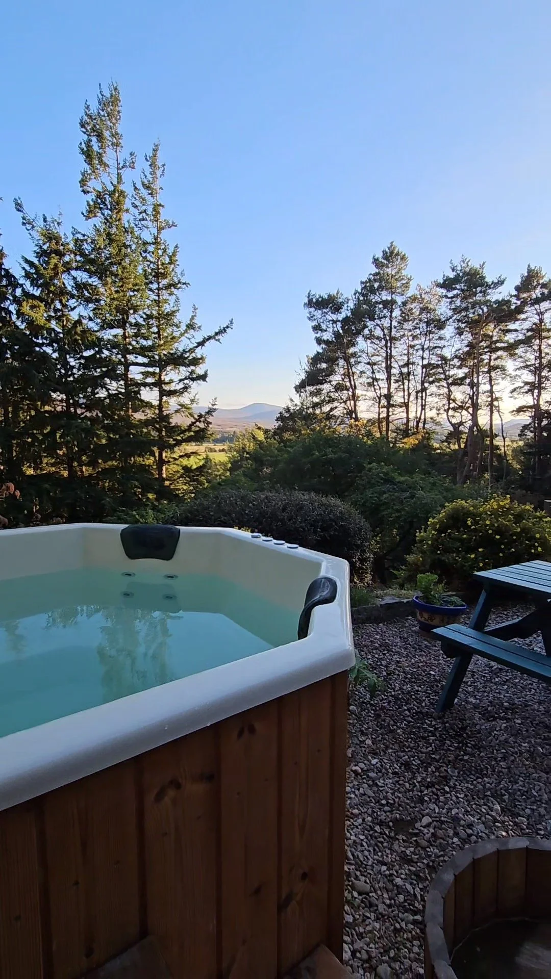 An outdoor hot tub with water, overlooking a landscape of trees and mountains during sunset.
