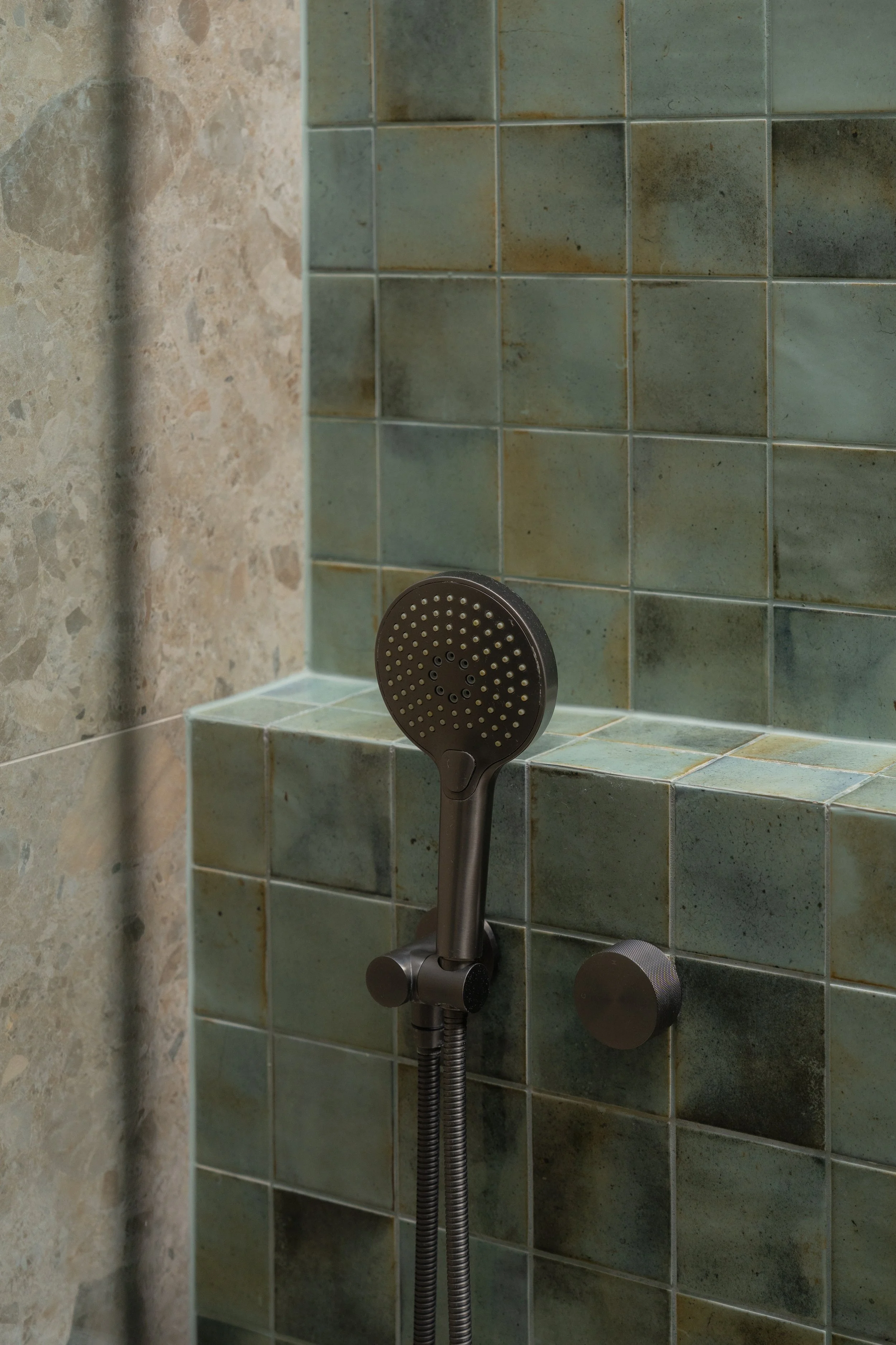 Showerhead and control knob in a tiled shower.