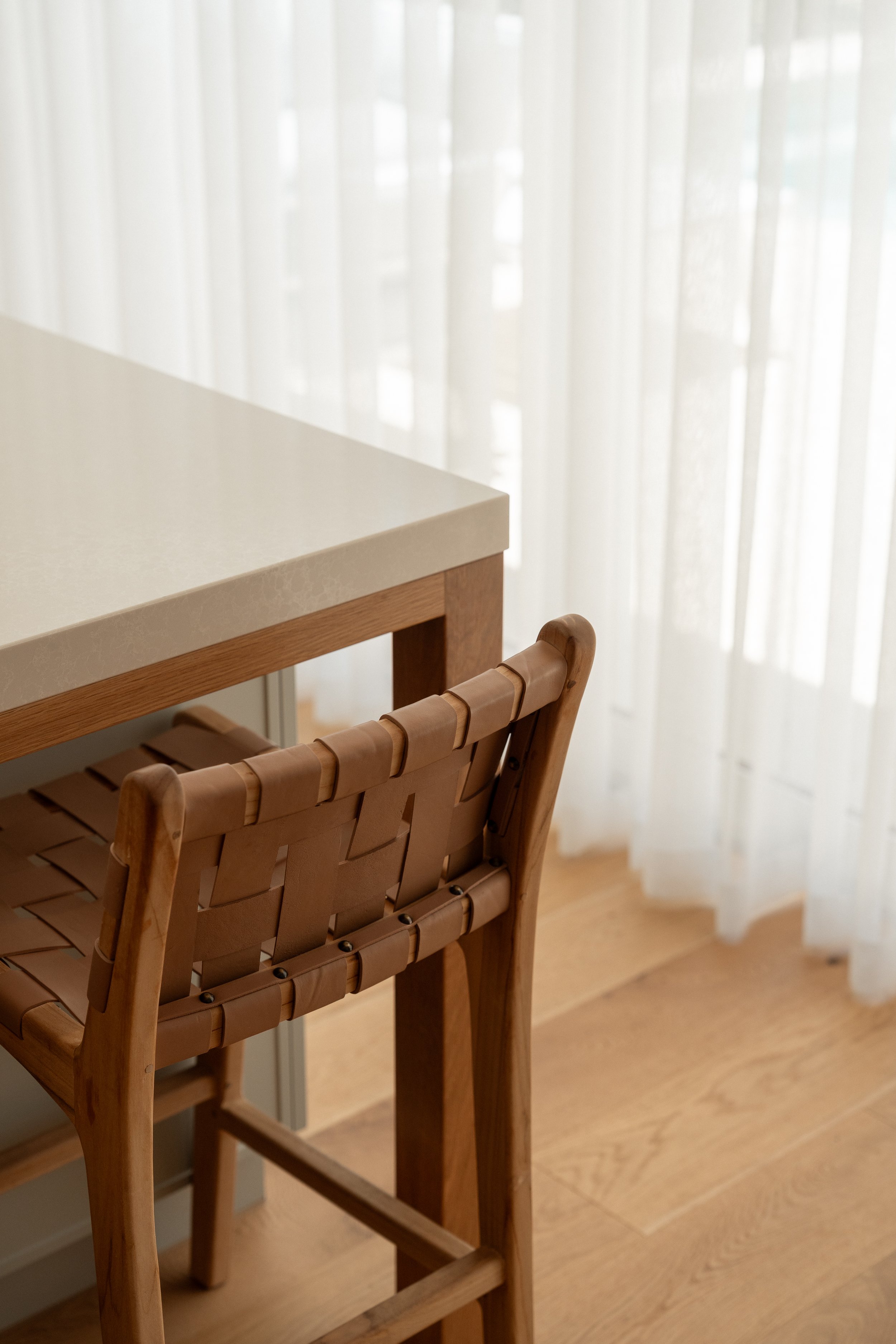 Wooden chair at a dining table near a sheer curtain with natural light.