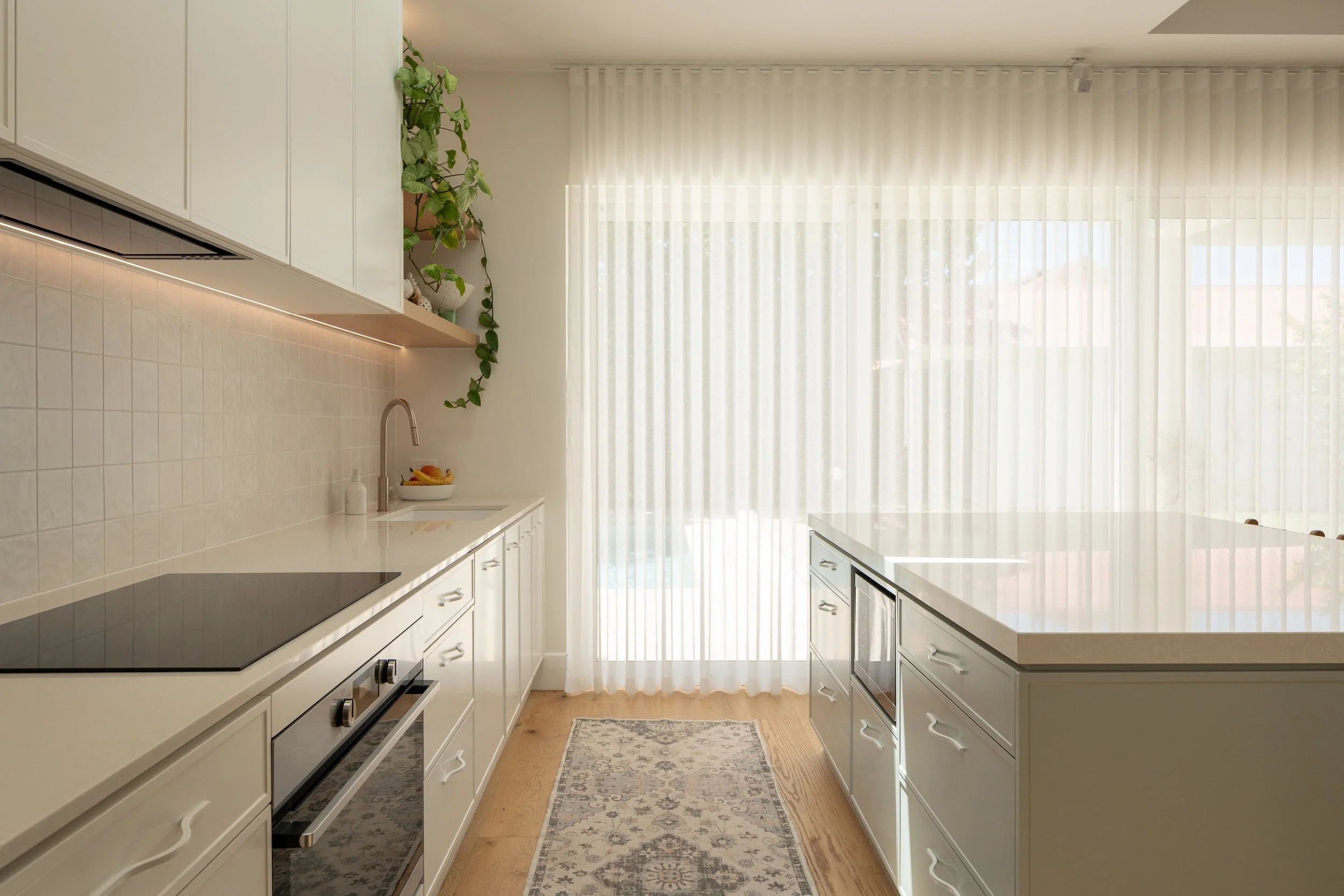 Bright modern kitchen with white cabinets, a kitchen island, and large window with sheer curtains.