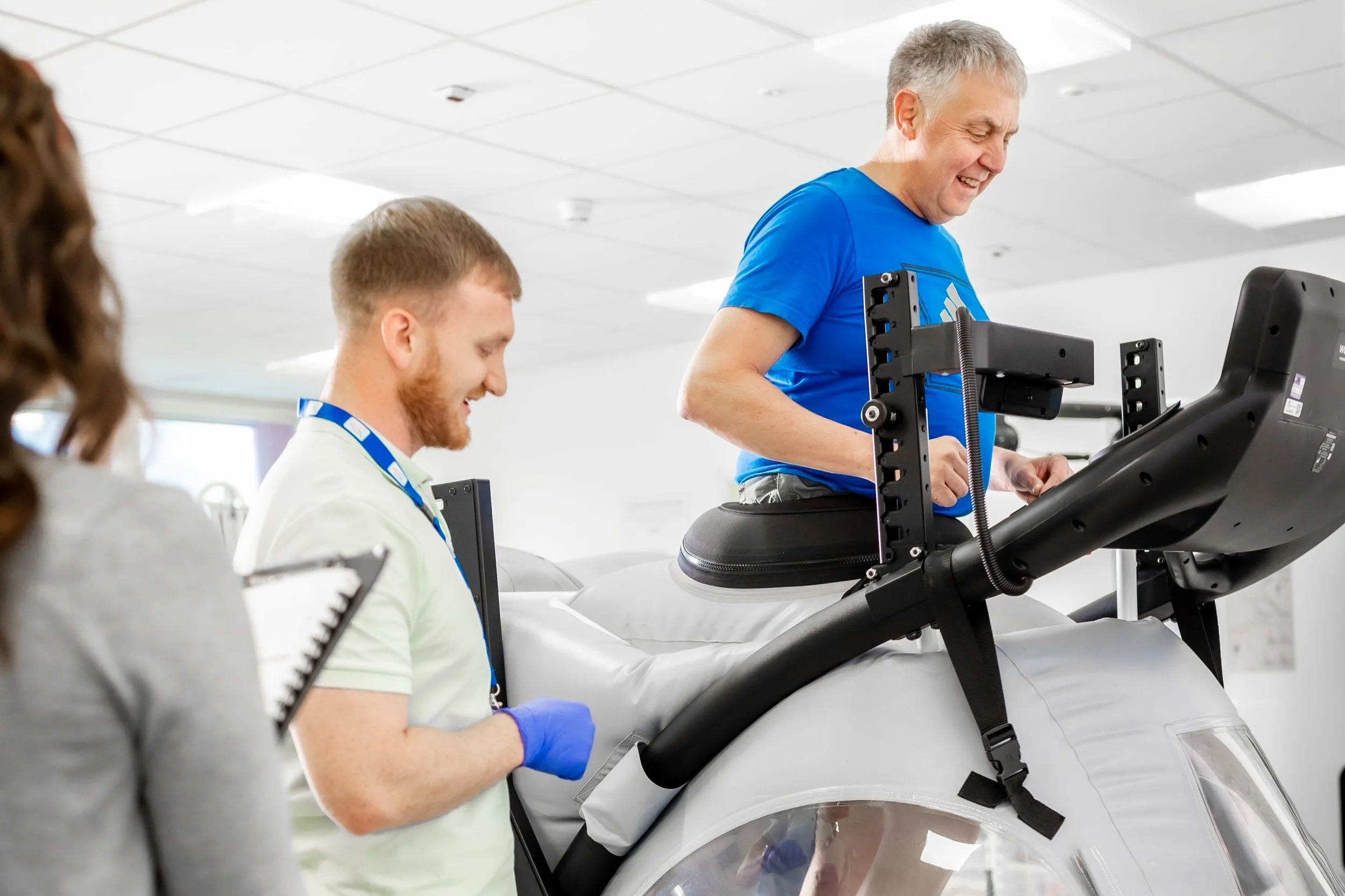 A man using an anti-gravity treadmill with a trainer assisting him.