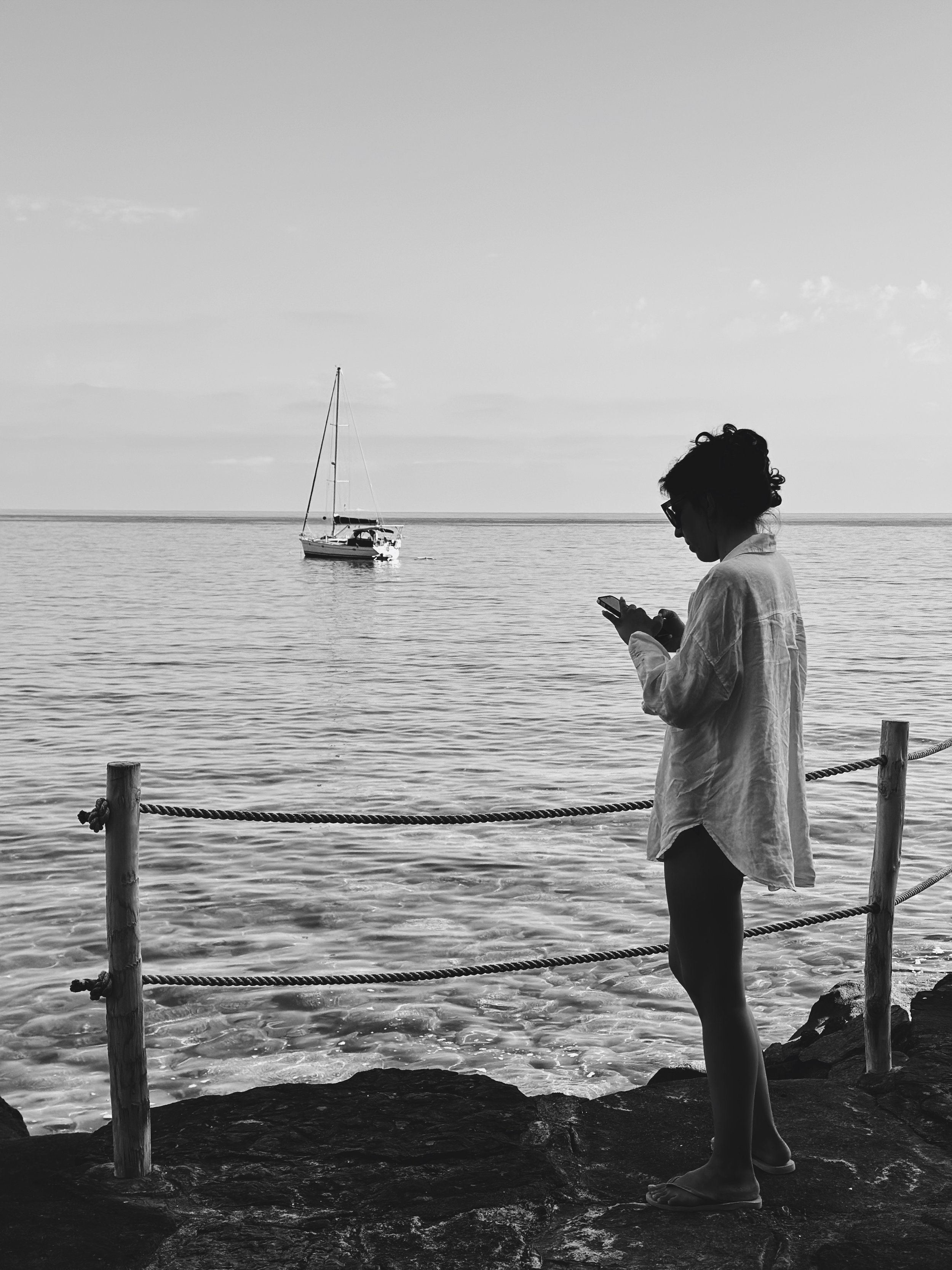 Woman looking over the ocean and boats holding phone