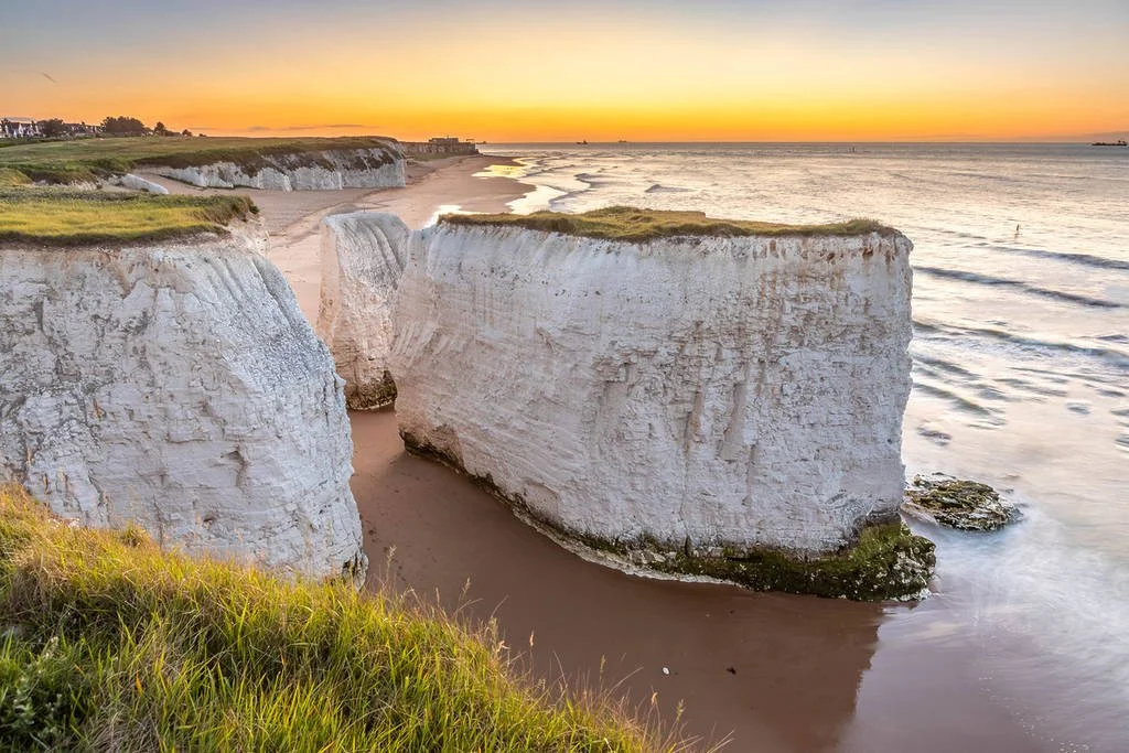 Golden hour over the white grass-topped cliffs of Botany Bay in the UK