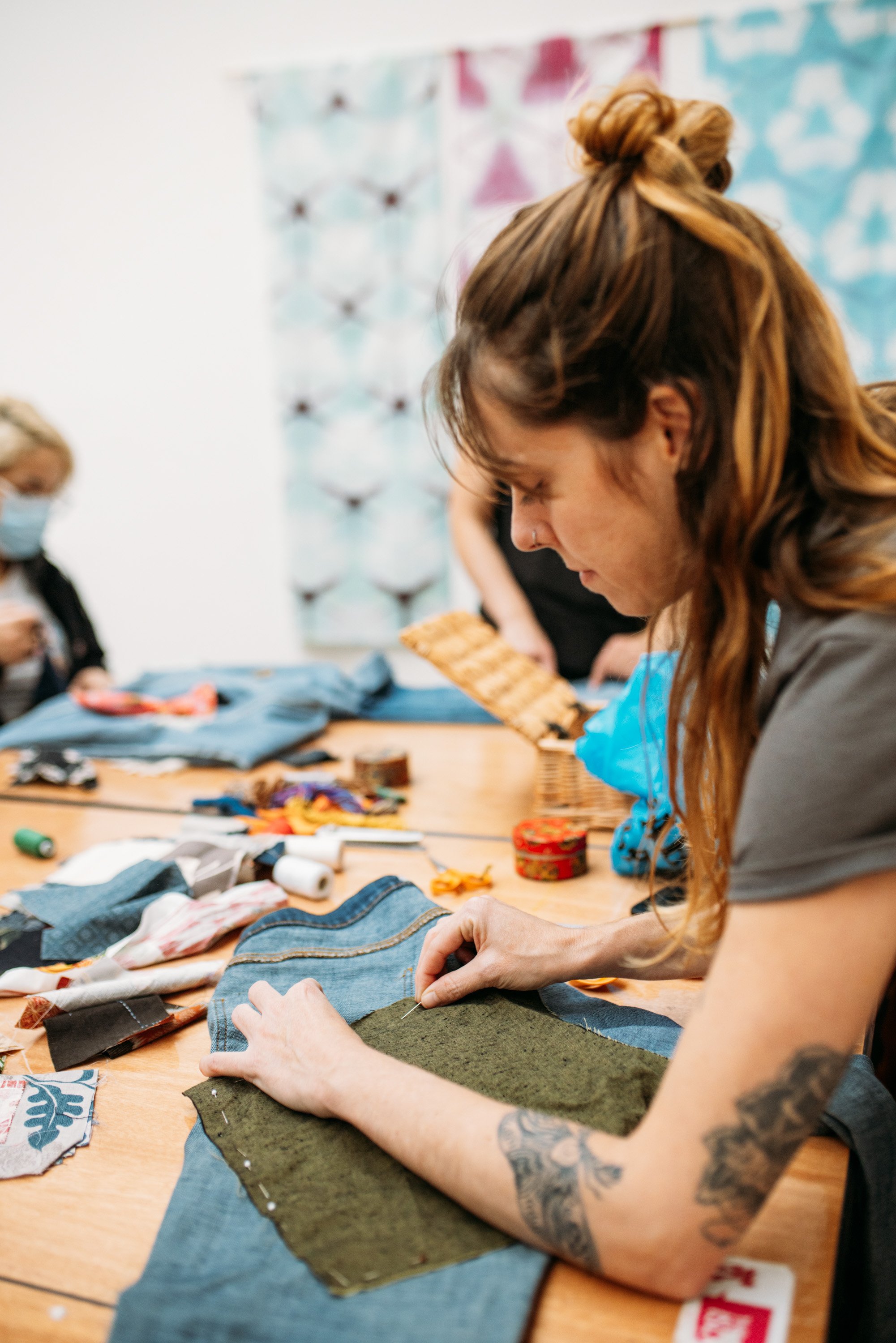Woman sewing fabric at a crafting table with sewing supplies and fabric scraps.