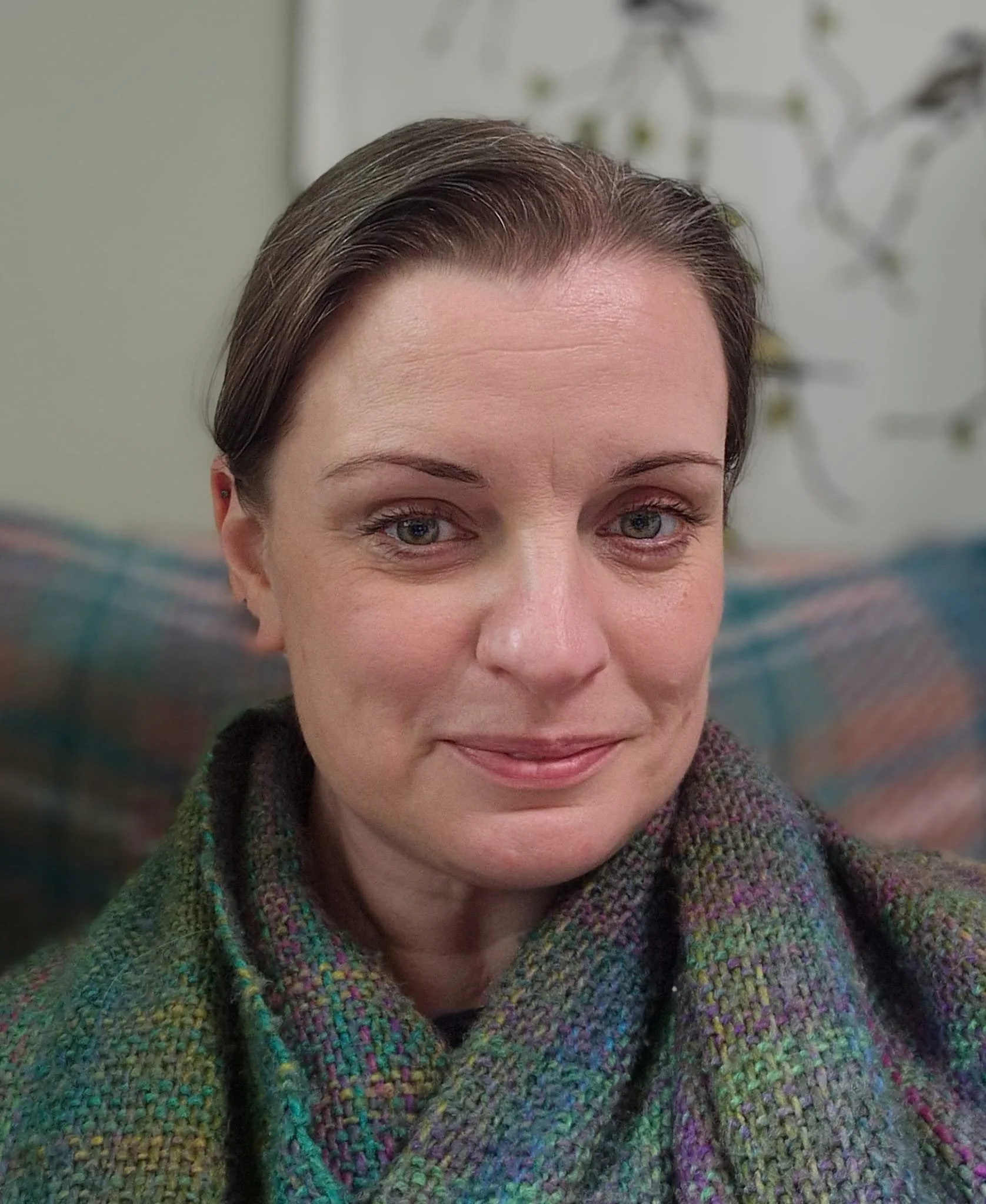 Close-up of a woman with short brown hair, green eyes, and light skin, wearing a multicolored woven scarf, in front of a neutral background.