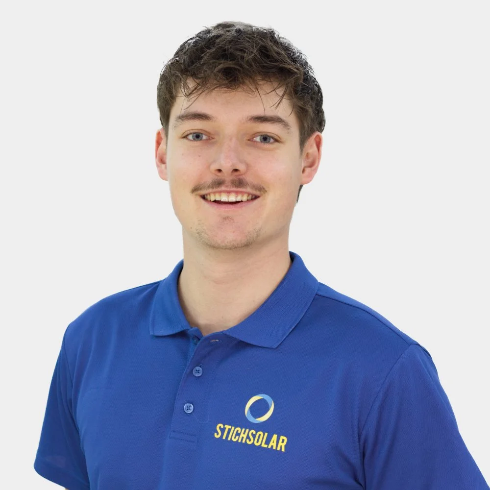 Junge Mann mit braunen, unordentlichen Haaren trägt ein blauen Polo-Shirt mit dem Logo 'STICHSOLAR' auf der Brust, lächelt vor weißem Hintergrund.