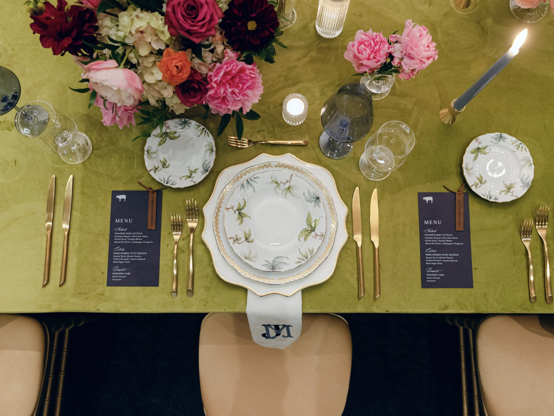 An olive green wedding table setting with vibrant pink flowers and gold utensils.