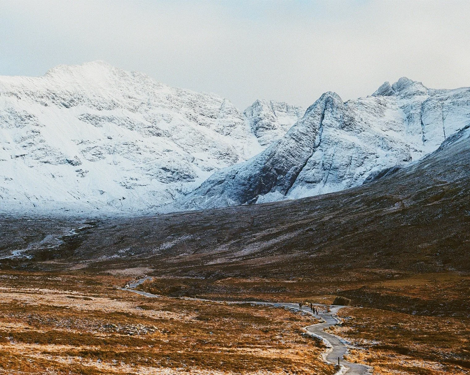 People walking on a small path in a valley towards snow-capped mountaints in the back