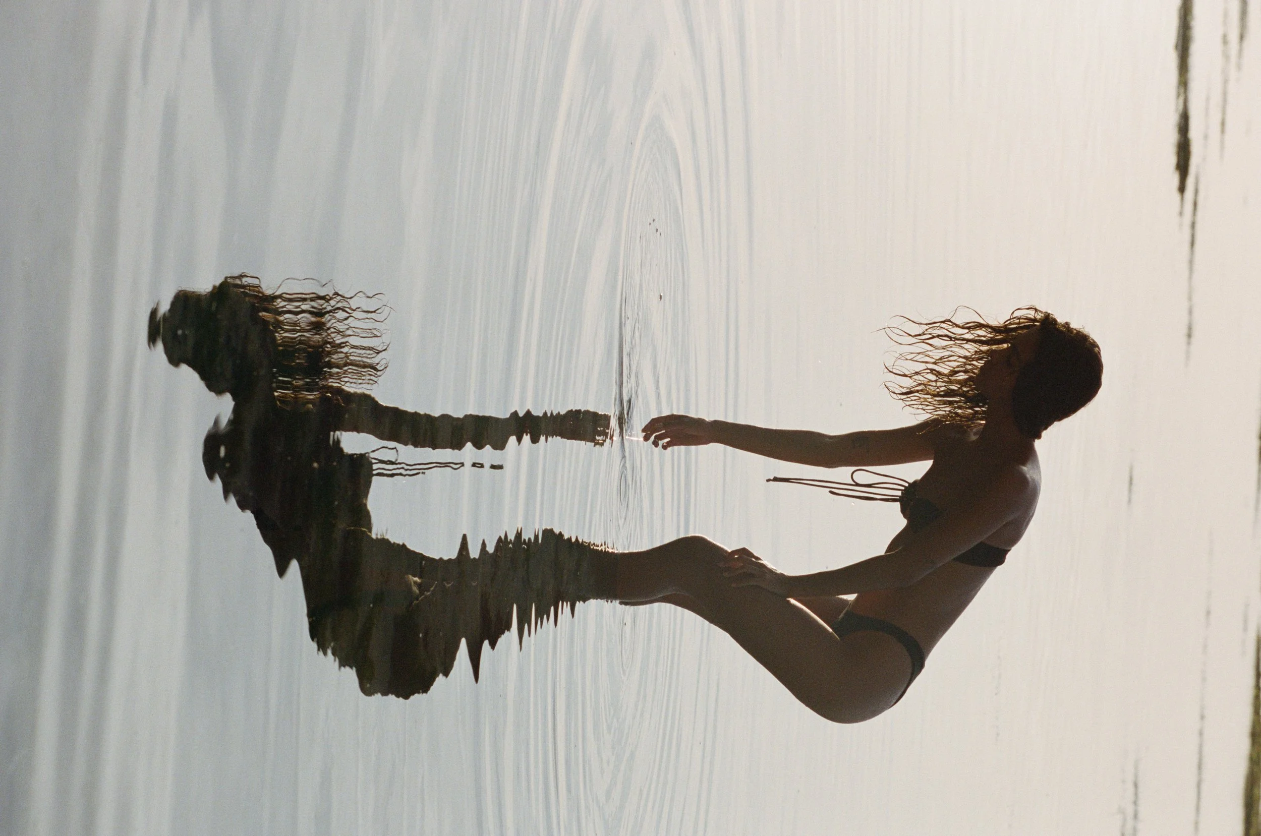 vertical image of a woman and her reflection in the ocean, touching the water