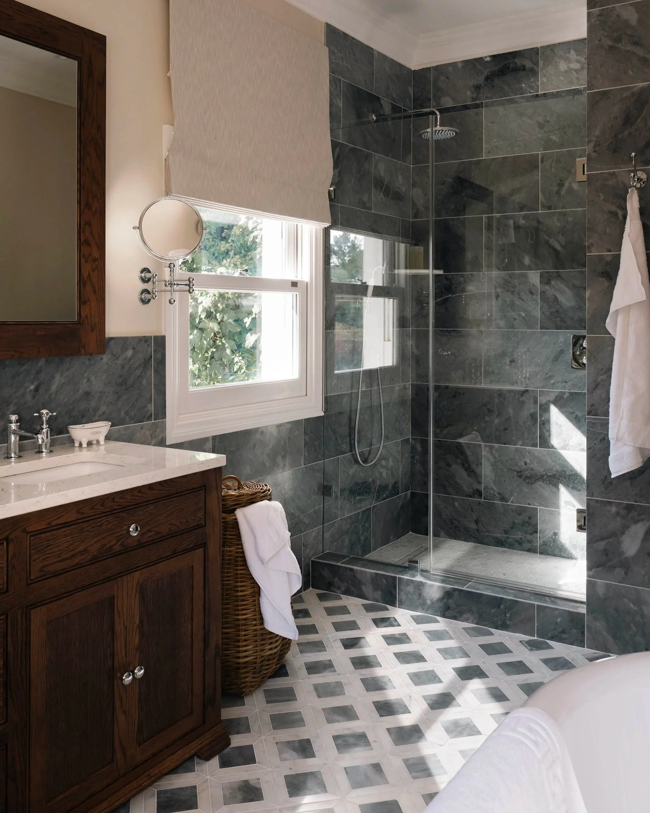 Master ensuite bathroom design featuring a dark wood vanity, walk-in shower enclosure with bluestone marble tiling, and geometric floor tiles.
