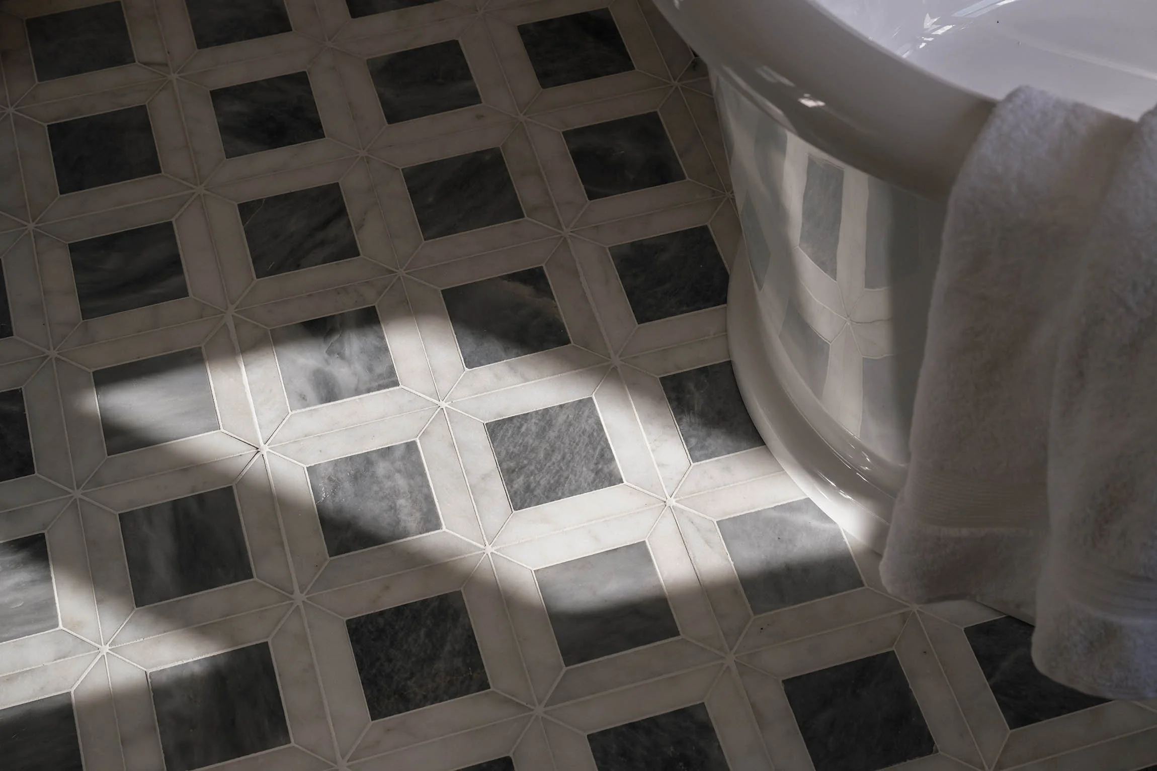 Detailed view of geometric blue and white marble floor tiles surrounding a freestanding bathtub in a Surrey master bathroom.