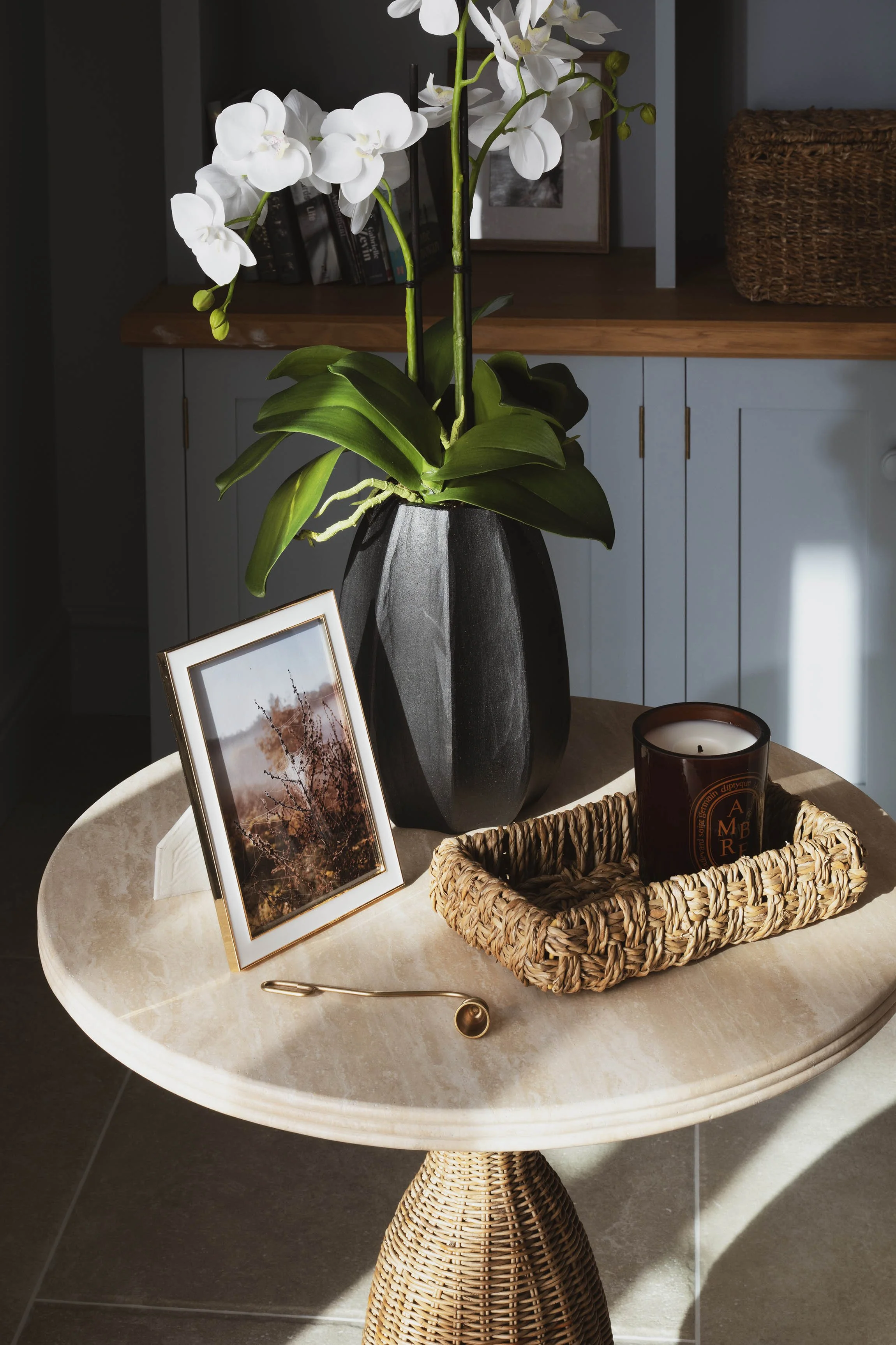 Elegant side table decor featuring an artificial orchid arrangement, woven tray, and luxury scented candle styled by Joanne Quinn Interiors.